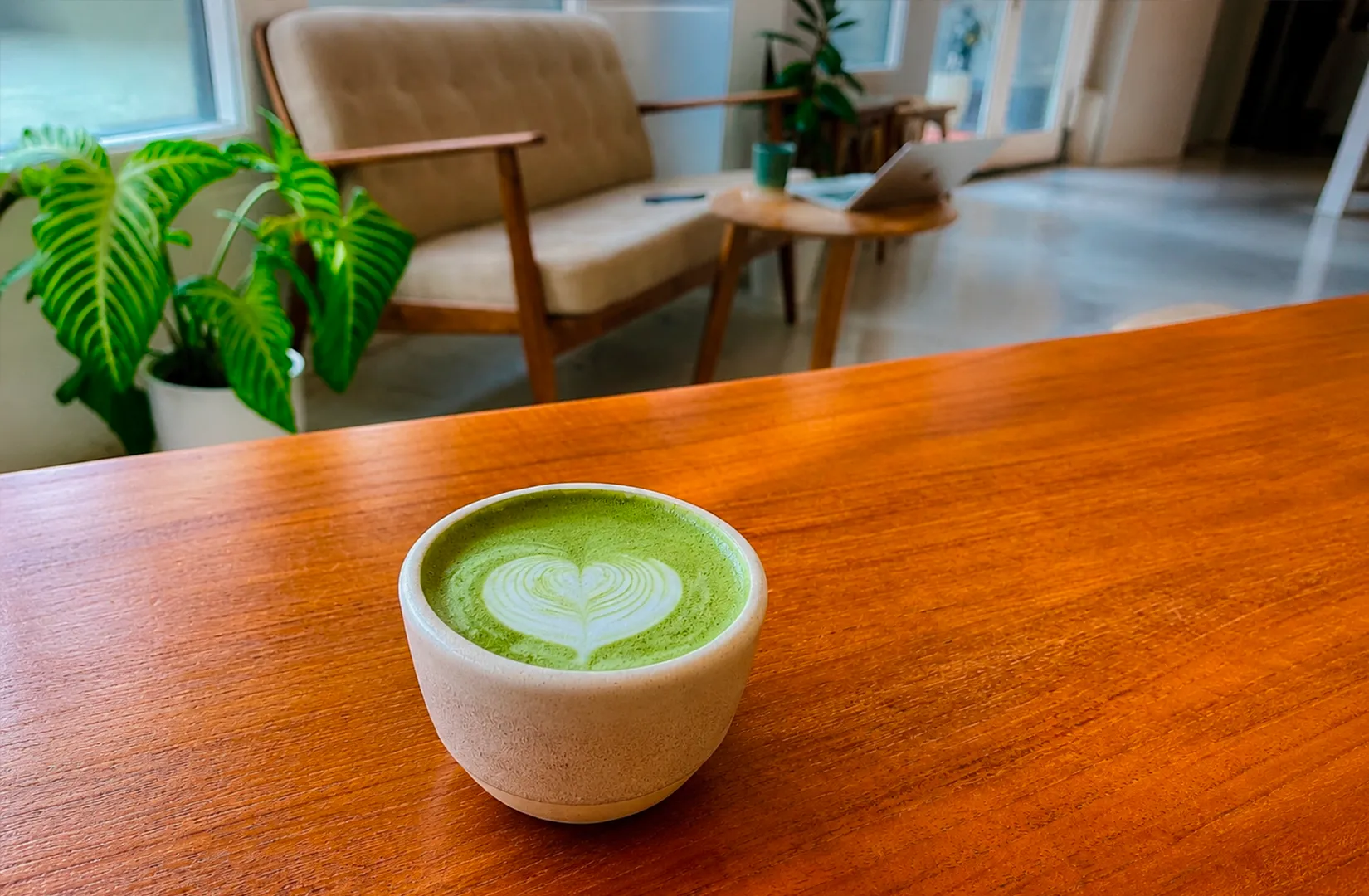 Ceramic cup of hot matcha latte with heart latte art on a wooden table in a cozy cafe