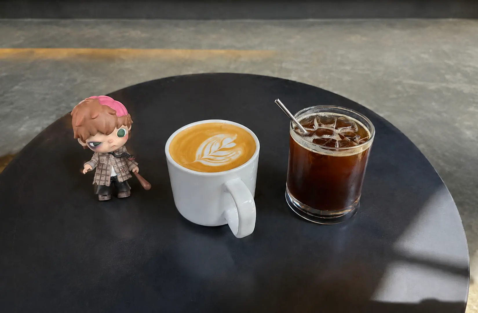 Latte and iced coffee served on a round table beside a small collectible figure.