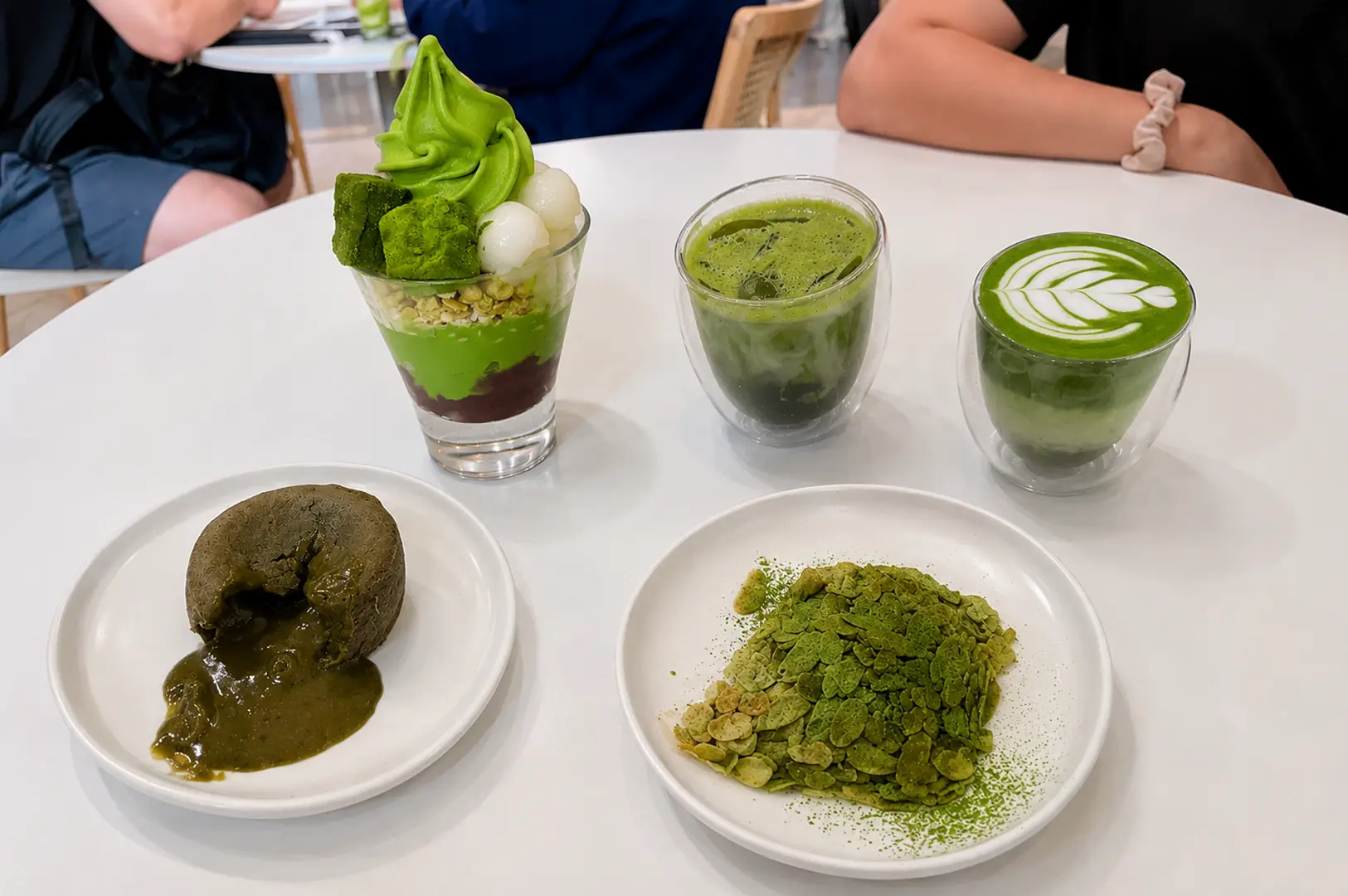 Table spread of matcha desserts including a parfait, lava cake, crisps, and matcha drinks at Matchaya