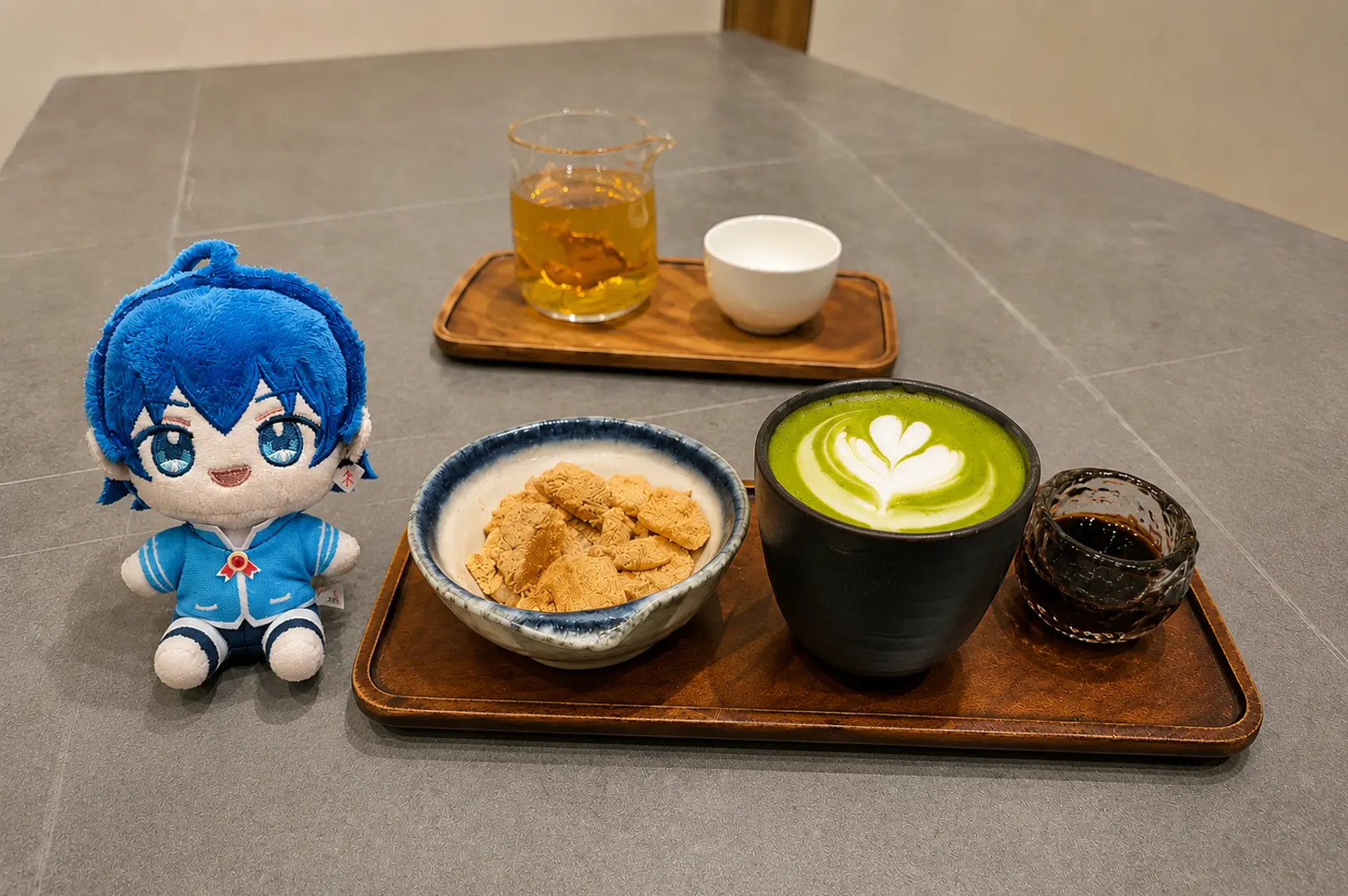 Hvala Matcha latte with latte art, cookies, and tea syrup on a wooden tray next to a blue plush doll