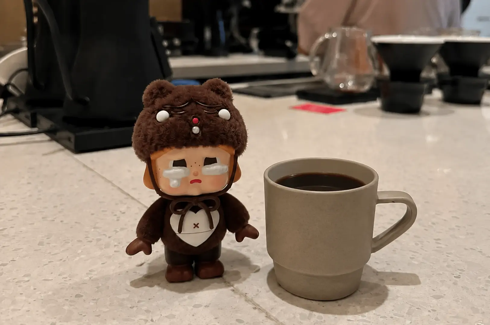 A brown bear collectible figurine stands beside a ceramic mug of hand drip coffee