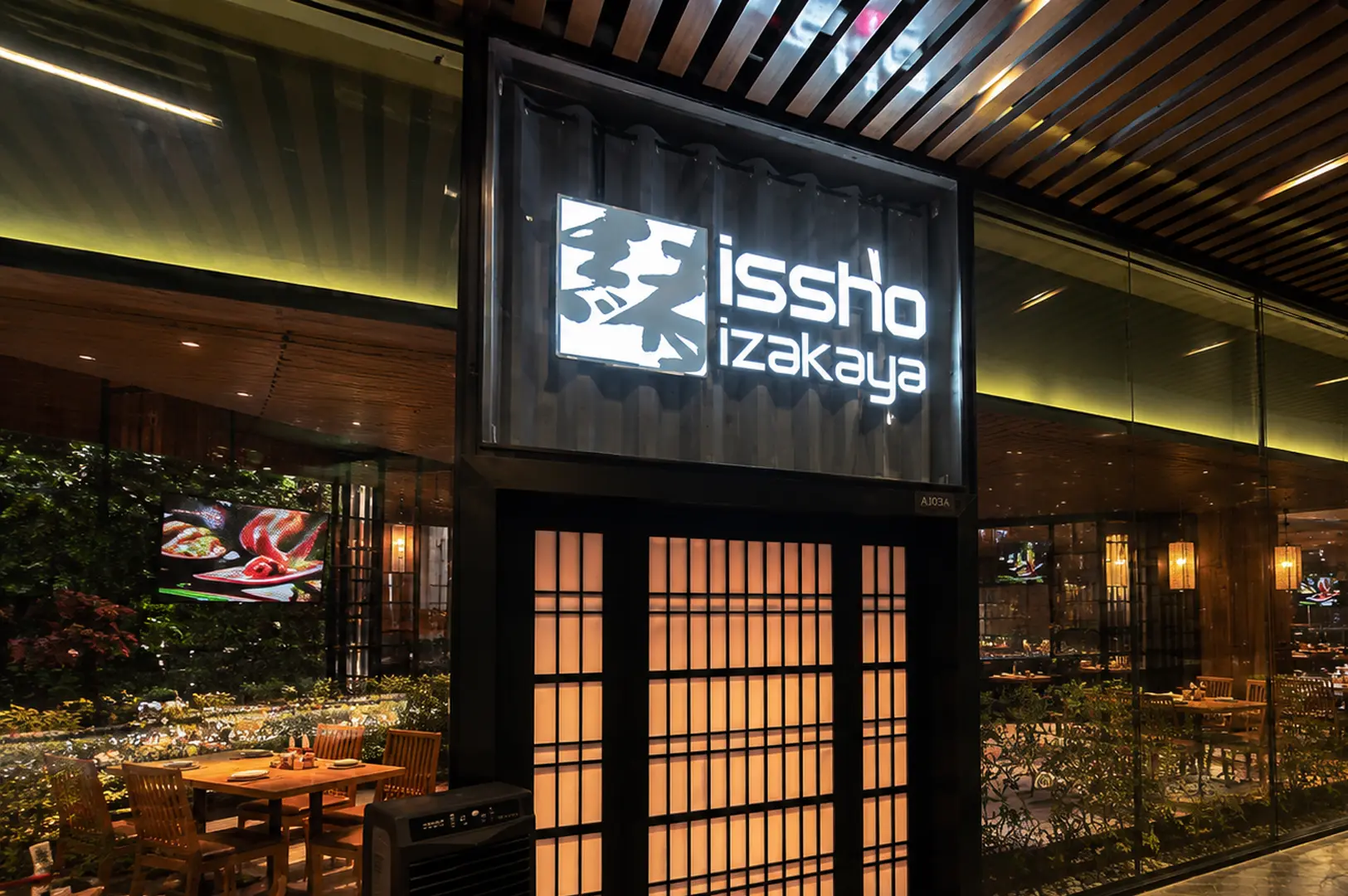 Exterior of Issho Izakaya featuring a modern black sign and illuminated shoji screen panels at the entrance with a wooden slat ceiling