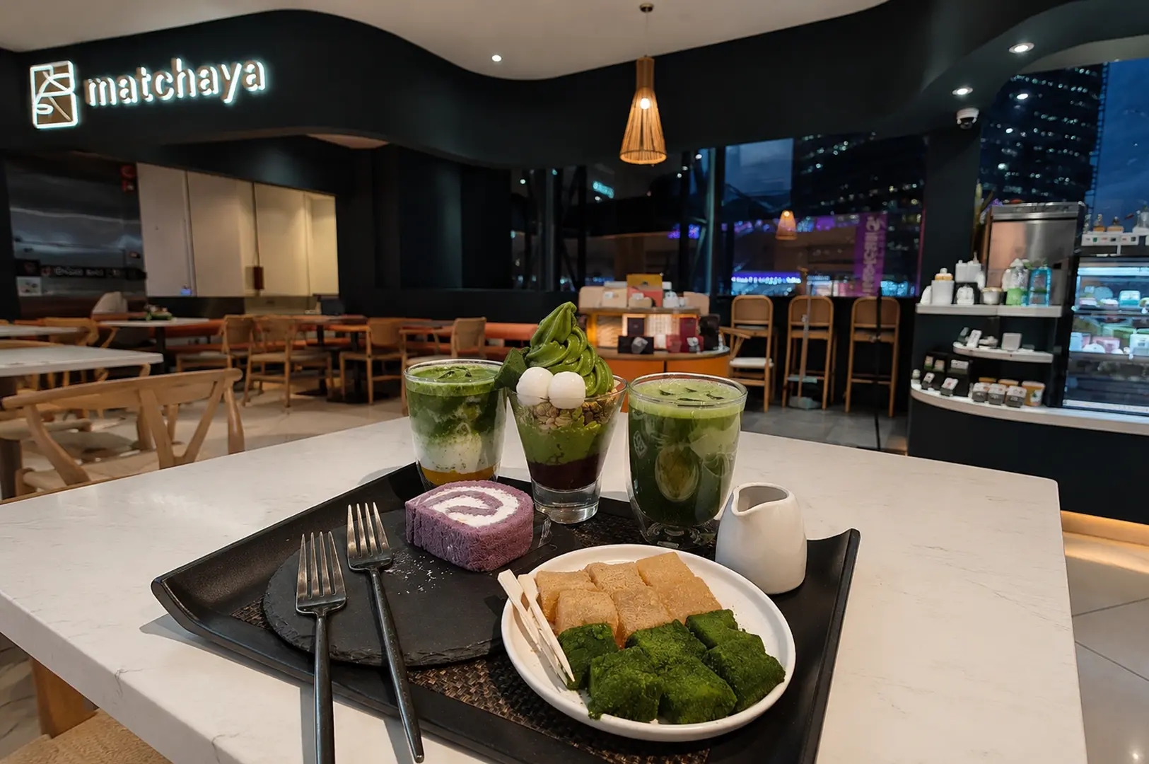 Table spread at Matchaya featuring layered matcha drinks, soft serve, purple swiss roll, and toast cubes