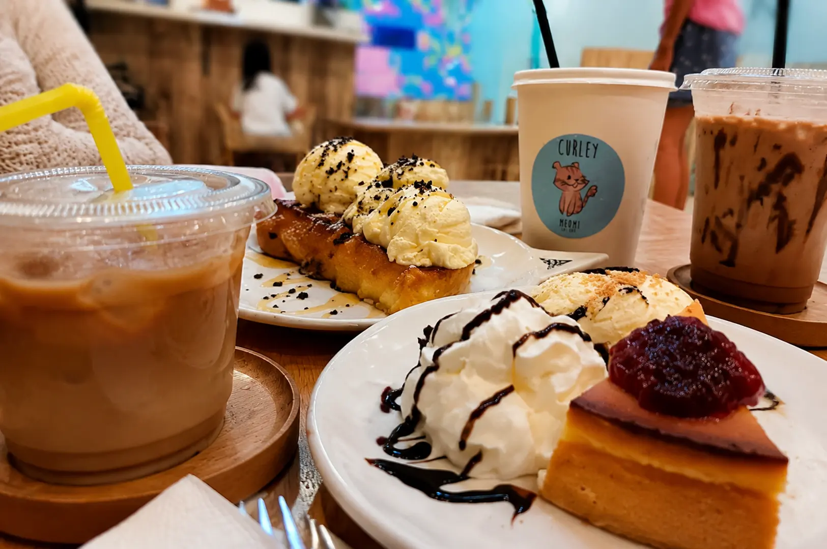 Waffles topped with vanilla ice cream, cheesecake, iced coffee, and chocolate drink served on a wooden table at Meomi Cat Cafe Singapore.
