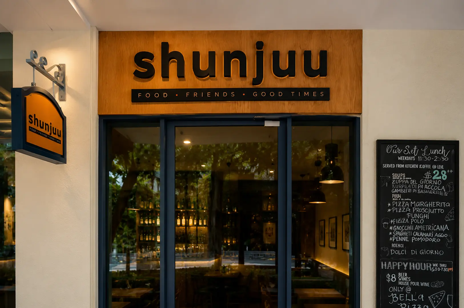 Storefront of Shunjuu restaurant with a wooden sign reading "Food Friends Good Times" and a chalkboard menu listing lunch specials