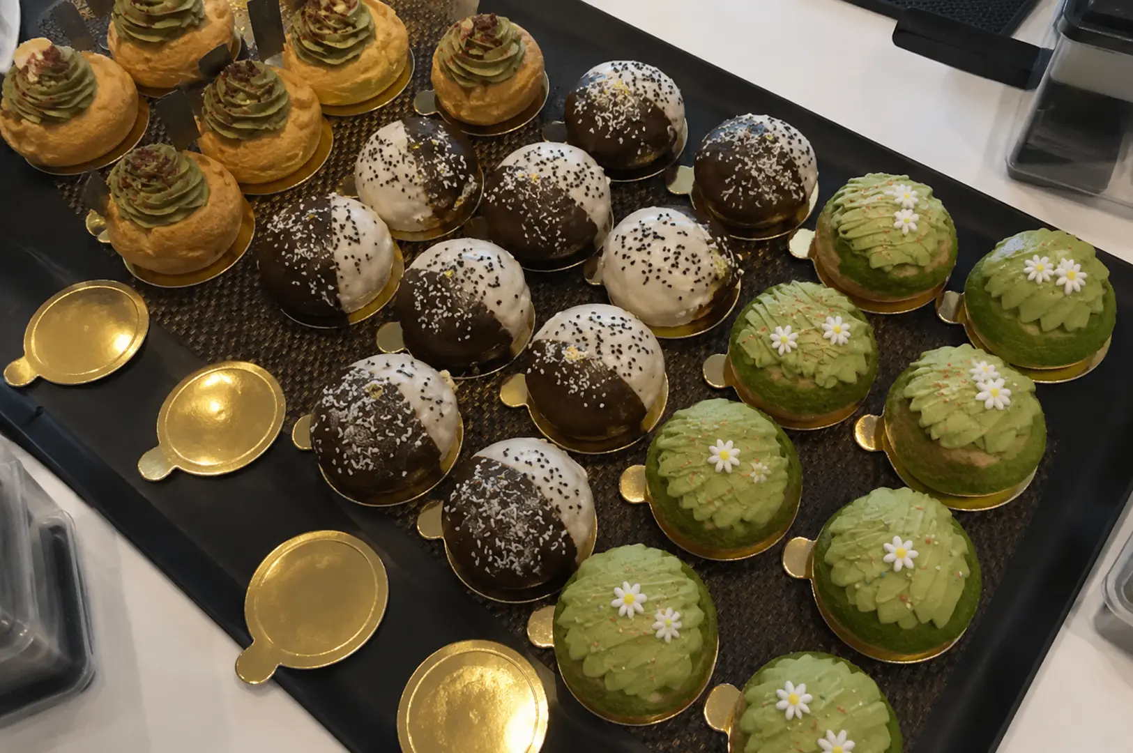 Black tray displaying assorted matcha pastries including cream puffs and decorated chocolate domes