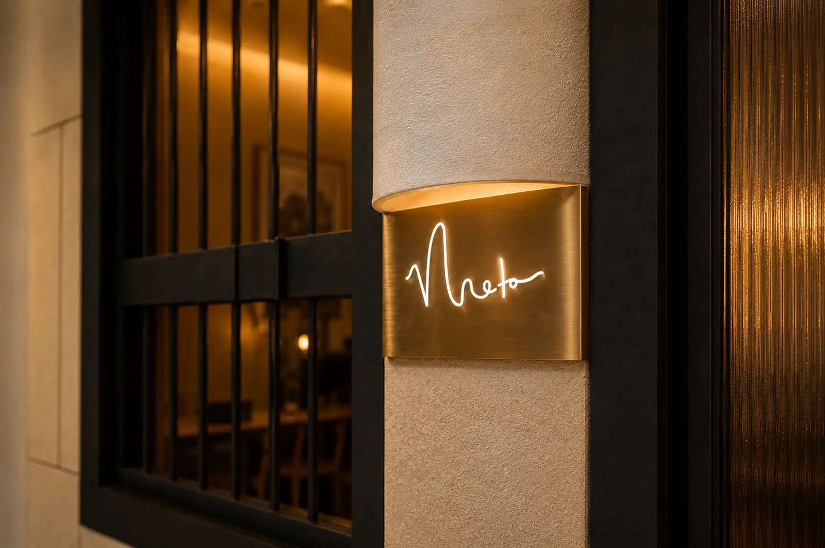 Brass plaque featuring the cursive neon logo of Meta restaurant mounted on a textured wall next to a black-framed window