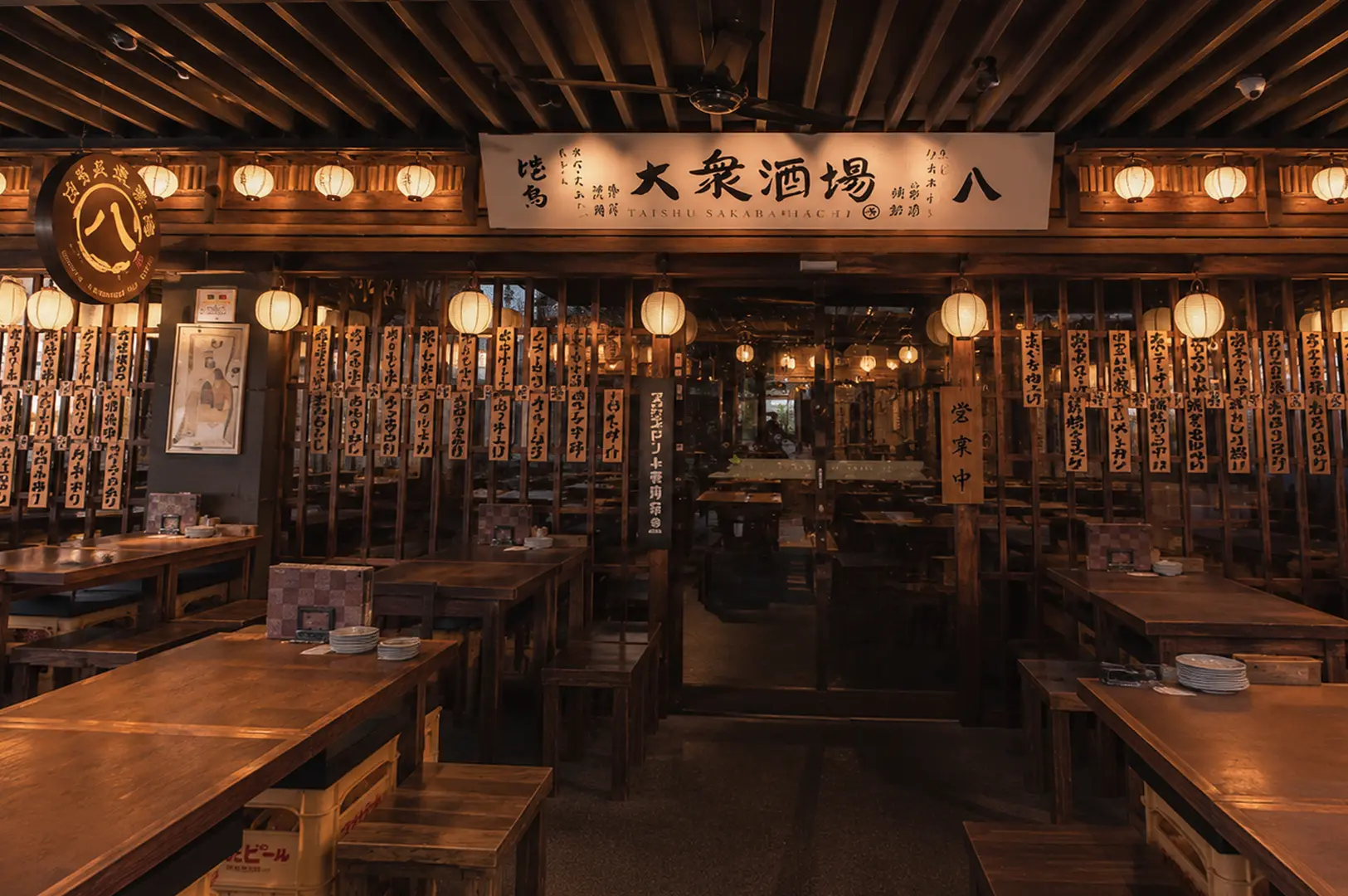 The Public Izakaya showing a rustic wooden design with hanging paper lanterns, traditional calligraphy banners, and wooden tables
