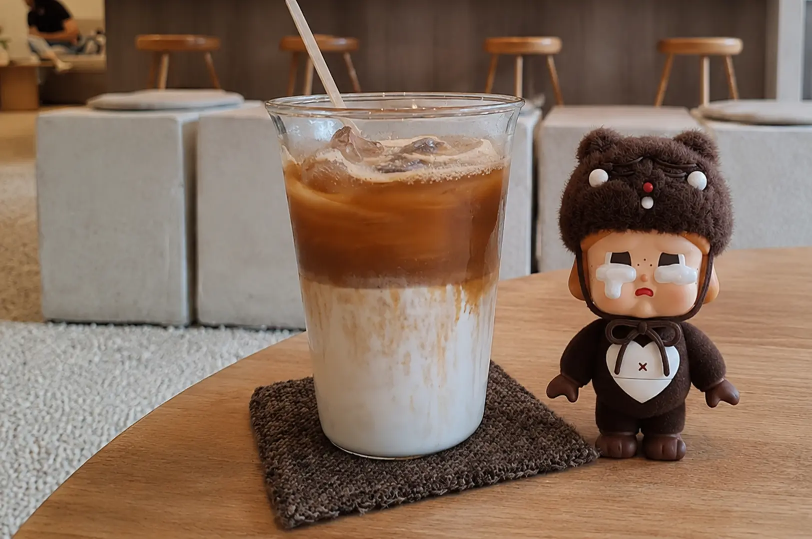 An iced latte sits on a wooden table next to a brown bear figurine at Kurasu cafe