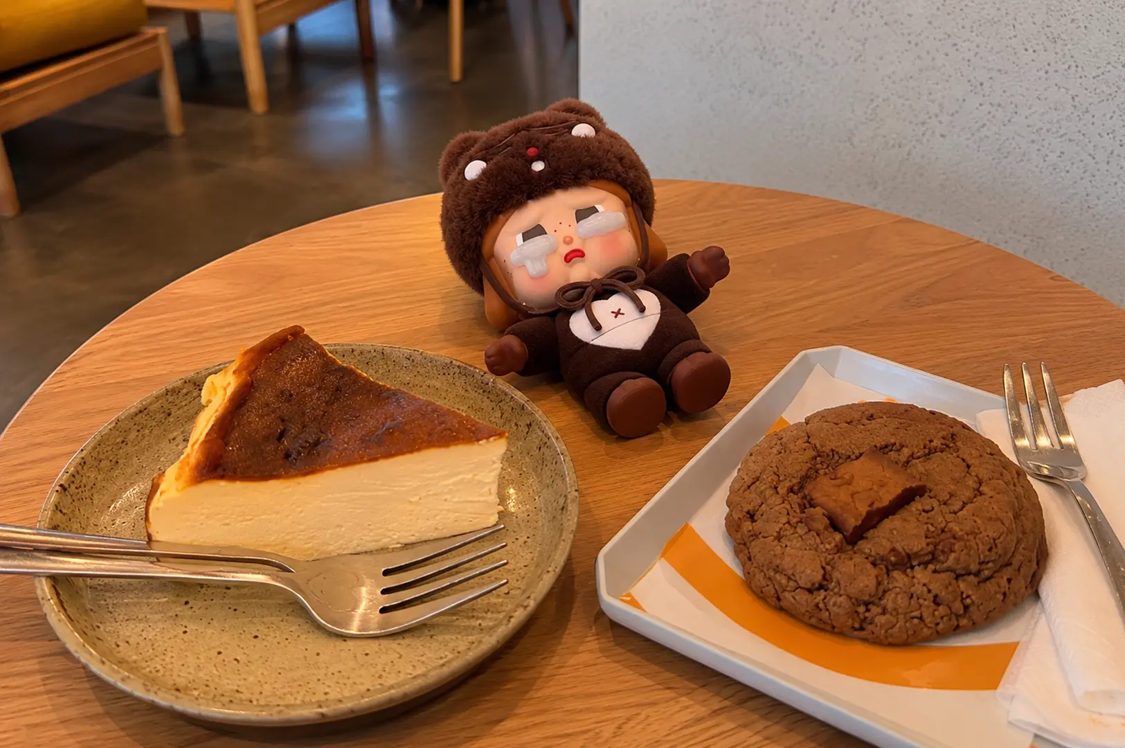 A slice of basque cheesecake and a chocolate cookie are served on a wooden table at Kurasu