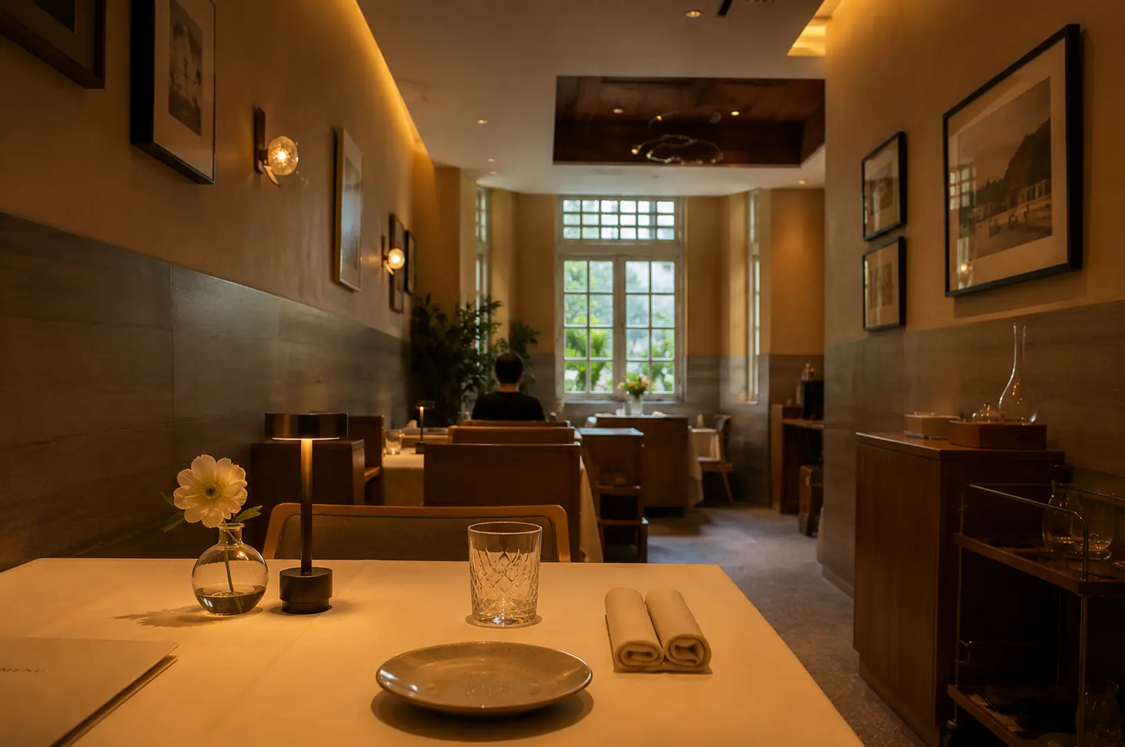 Elegant fine dining interior with warm lighting, framed artwork, and a neatly set table featuring a single white flower in a glass vase