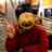 A person in a red hoodie holding up a piece of shumai dumpling with a funny mustache doodle overlay in a restaurant setting