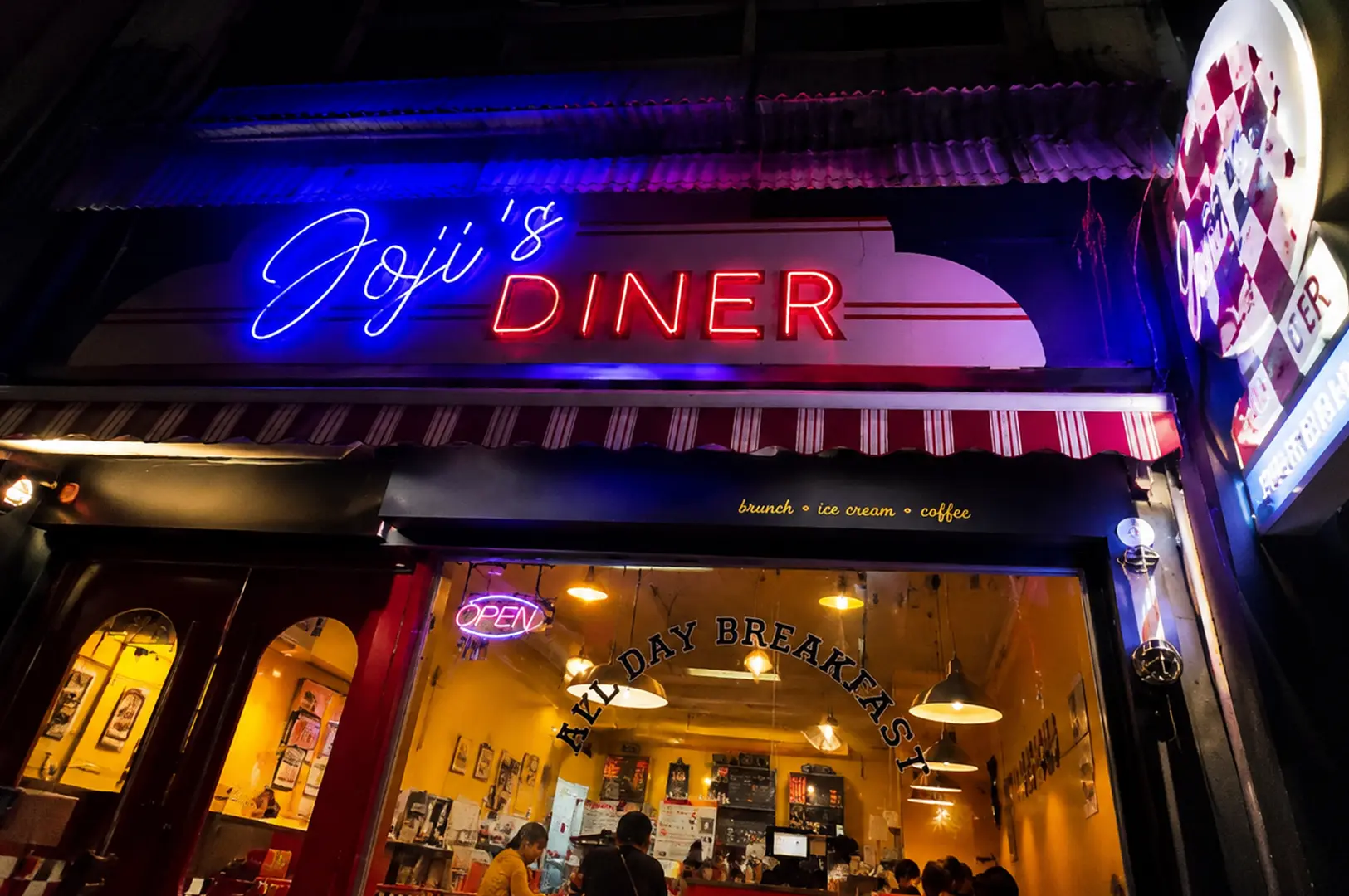 Joji’s Diner storefront glowing with blue and red neon lights at night in Serangoon.