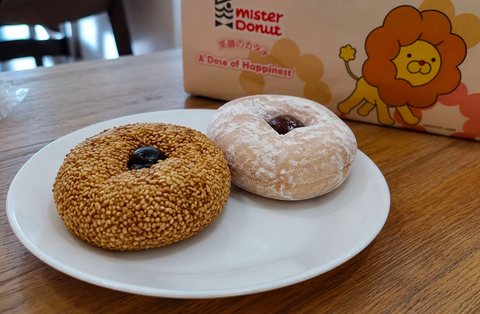 Mocchurin Red Bean and Double Sesame donuts served on a white plate with a Mister Donut box on a wooden table.