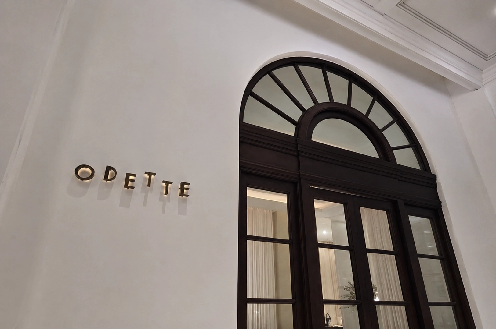 Exterior entrance of Odette Singapore showcasing the elegant arched doorway, minimalist façade, and iconic restaurant signage.