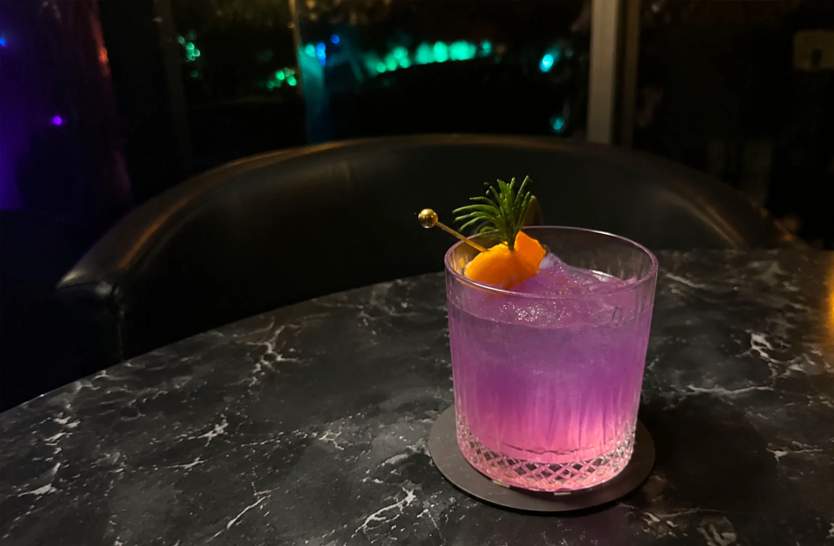 Purple astrology cocktail with citrus garnish on a marble table.