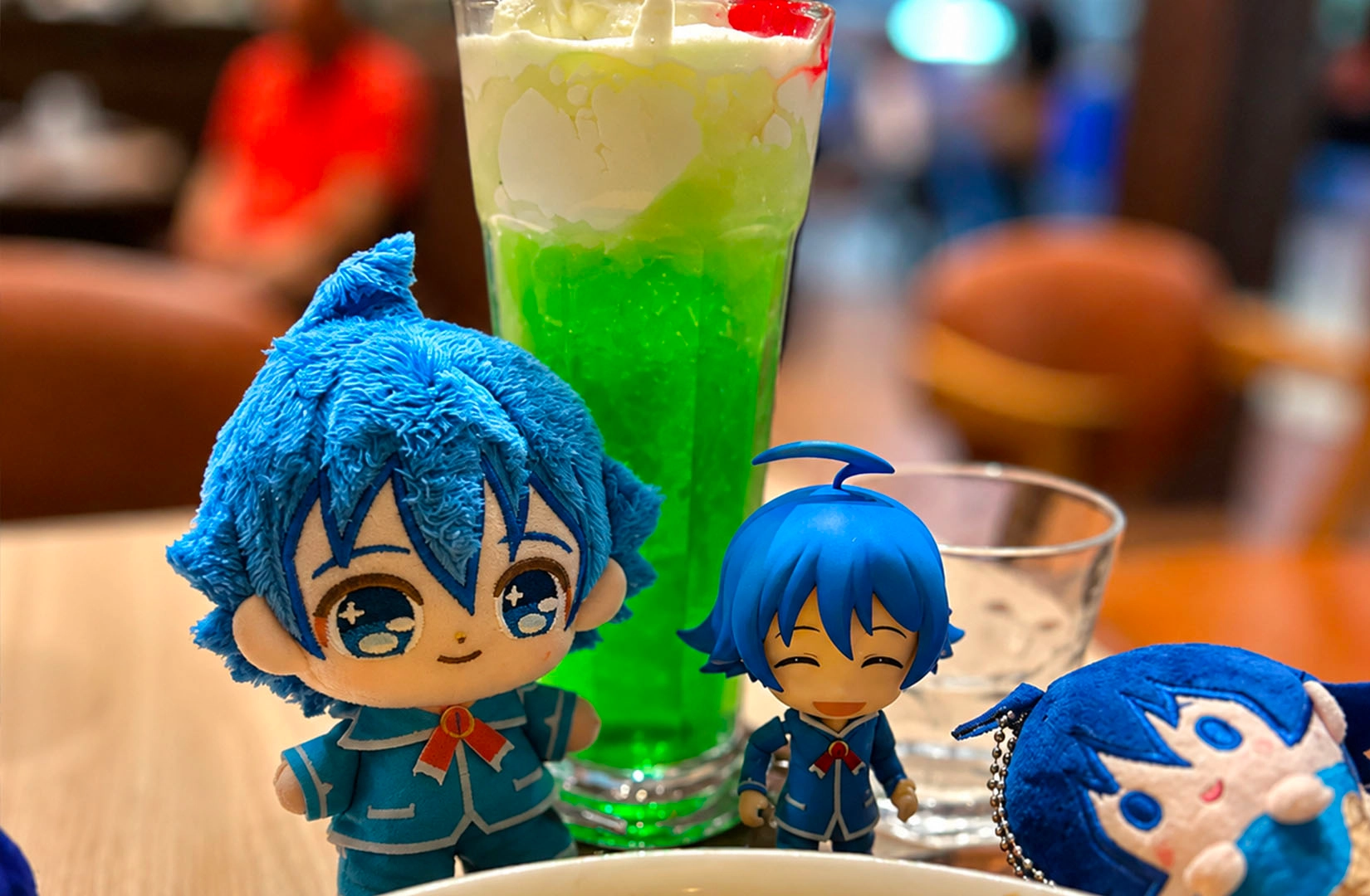Blue anime plush beside green cream soda float in a café