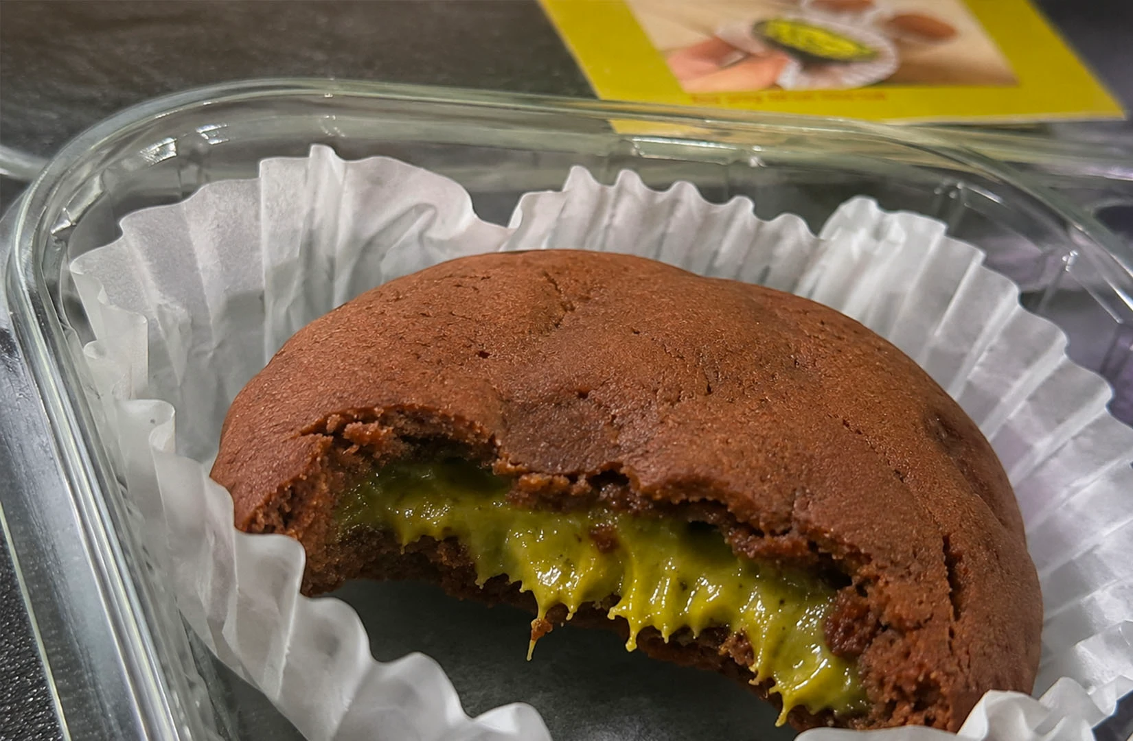 A chocolate cookie with a bite taken out shows a gooey green pistachio cream filling oozing from the center