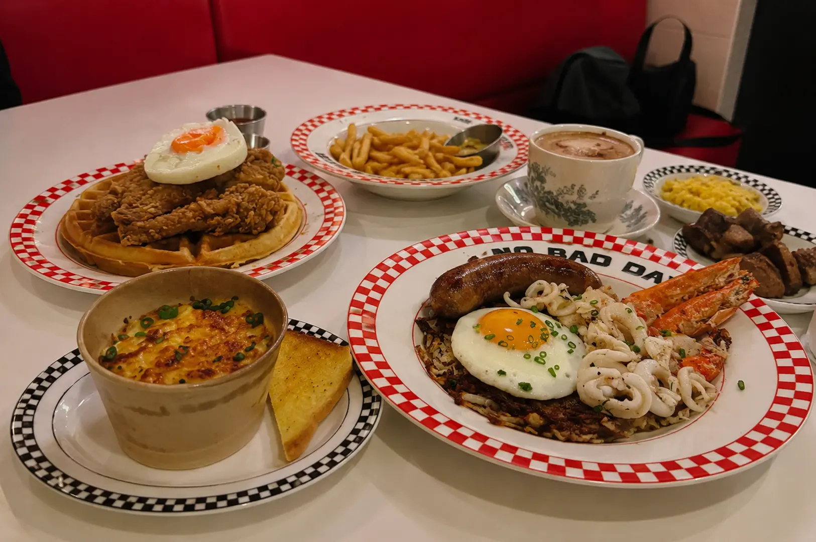 A table filled with Joji’s Diner dishes, including chicken and waffles, seafood rice, fries, baked eggs, and coffee.