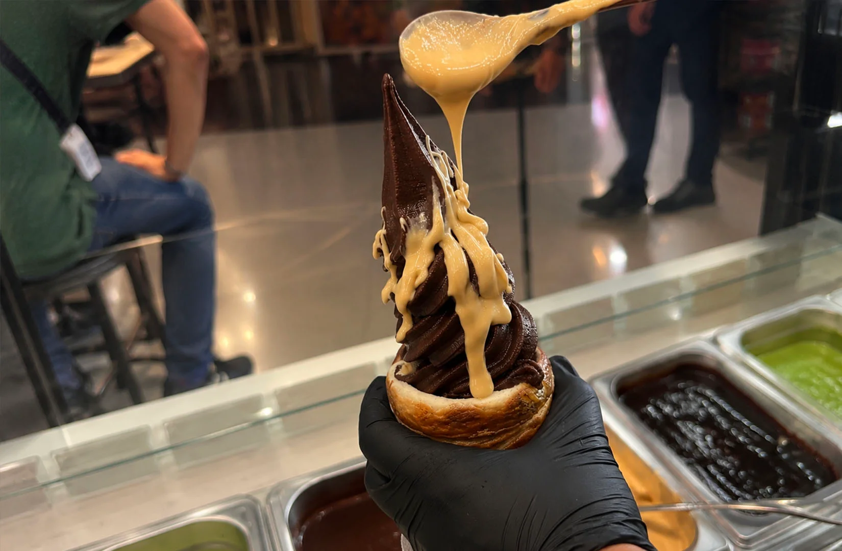 Chocolate soft serve on kurtos with creamy sauce being poured over