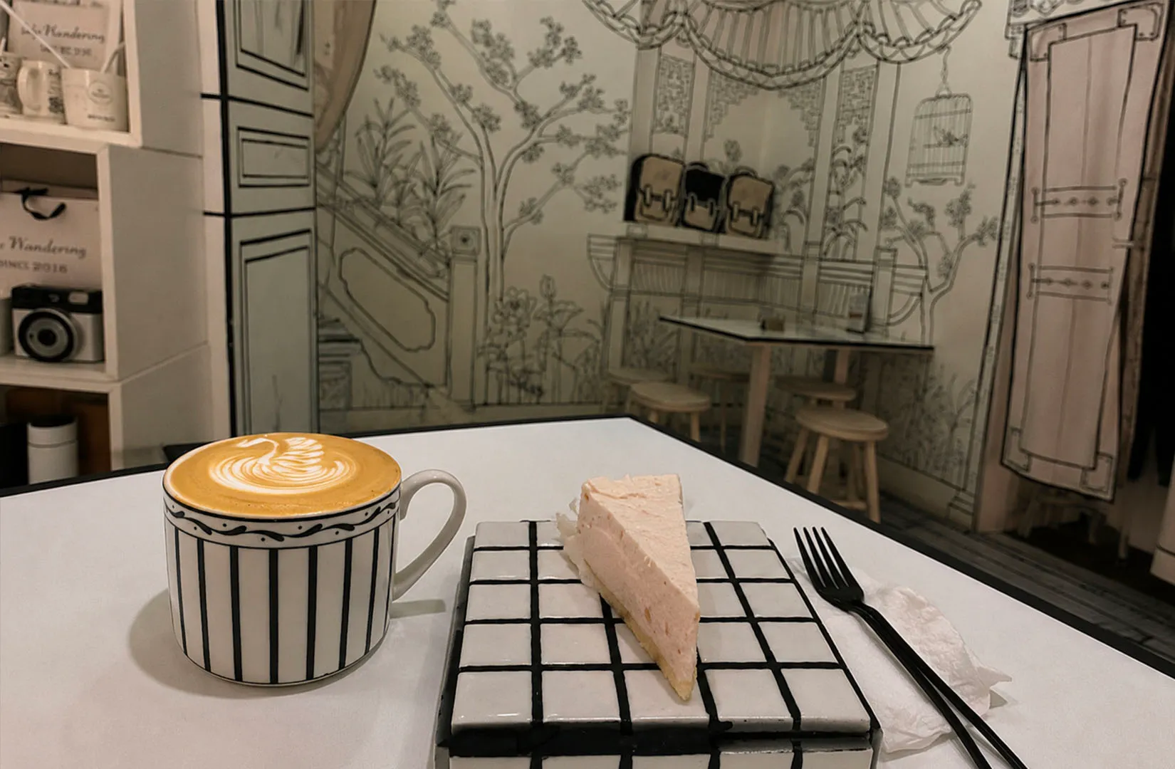 Minimal cafe table with latte art coffee and a slice of cake on a patterned plate.