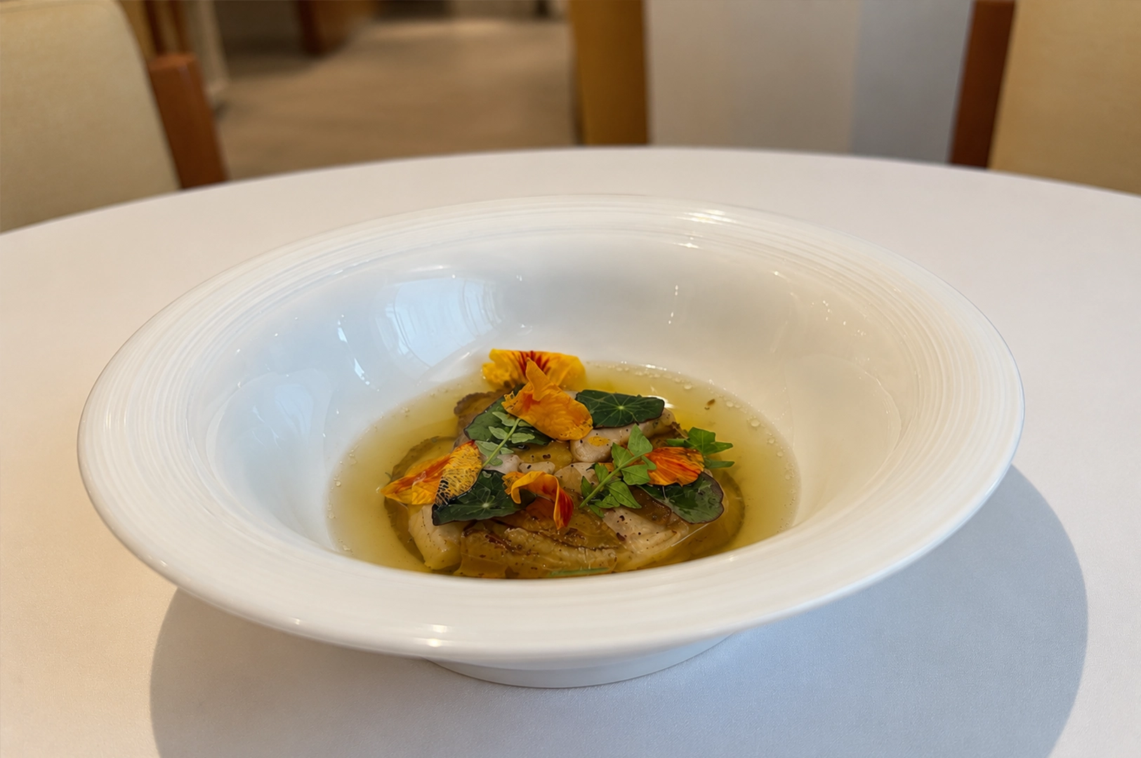 Jeju abalone with foie gras and pork broth beautifully plated in a deep white bowl with edible flowers and delicate herbs.