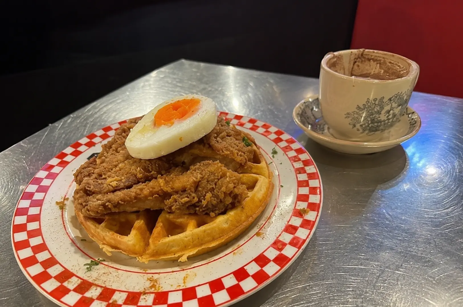 Crispy fried chicken and waffles topped with an egg, served with a cup of hot chocolate at Joji’s Diner.