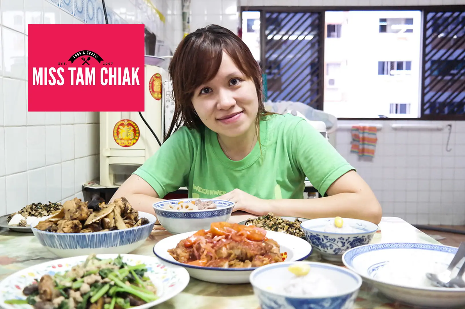 Miss Tam Chiak smiling warmly behind a table laden with an array of home-cooked dishes in blue and white porcelain bowls