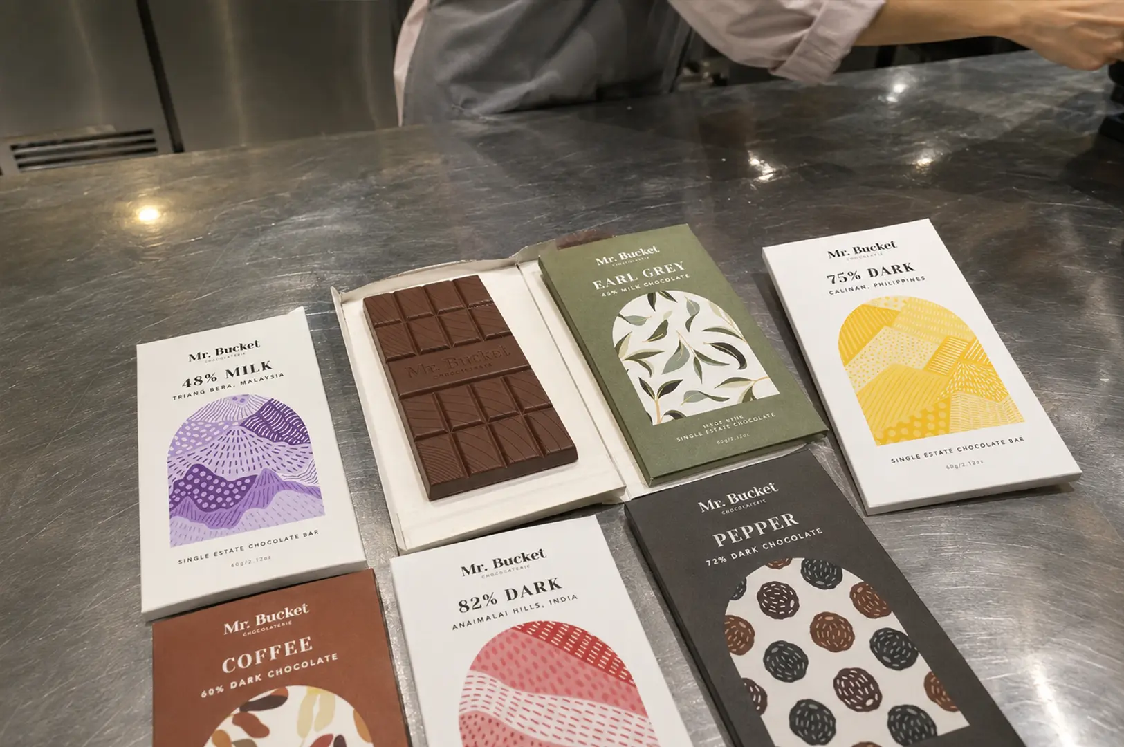 Selection of handcrafted single-origin chocolate bars displayed on a worktable inside Mr. Bucket Chocolaterie, highlighting unique flavors and origins.