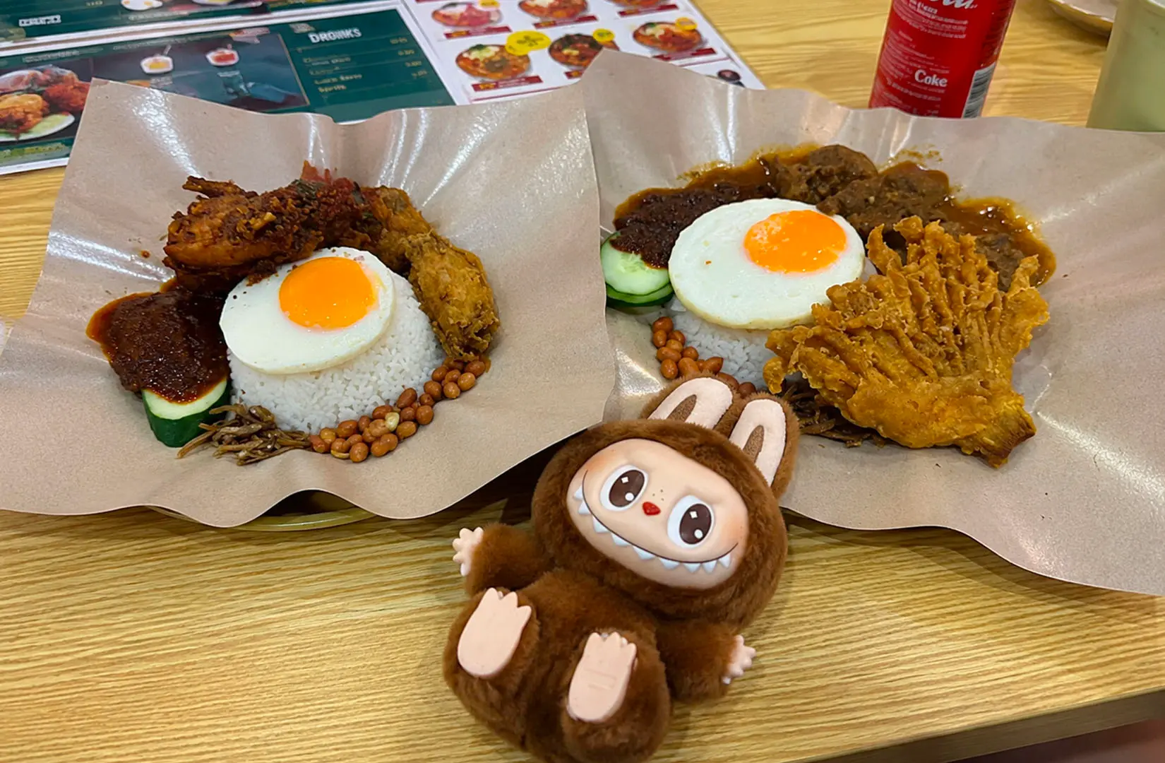 Nasi lemak with fried chicken, egg, sambal, and drinks on a restaurant table