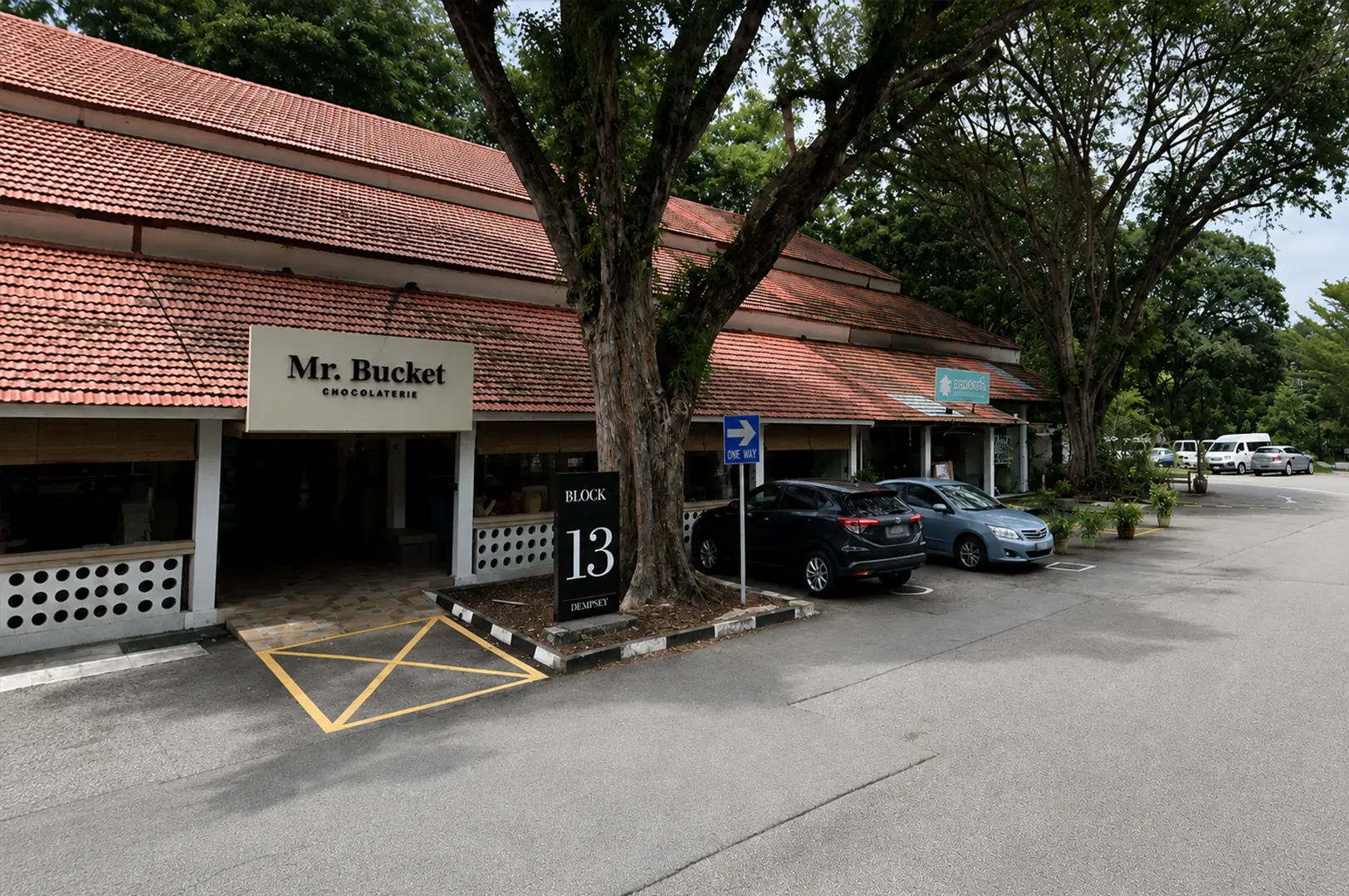 Exterior daytime view of Mr. Bucket Chocolaterie nestled among lush trees at Dempsey Hill, home to handcrafted bean-to-bar chocolate experiences.