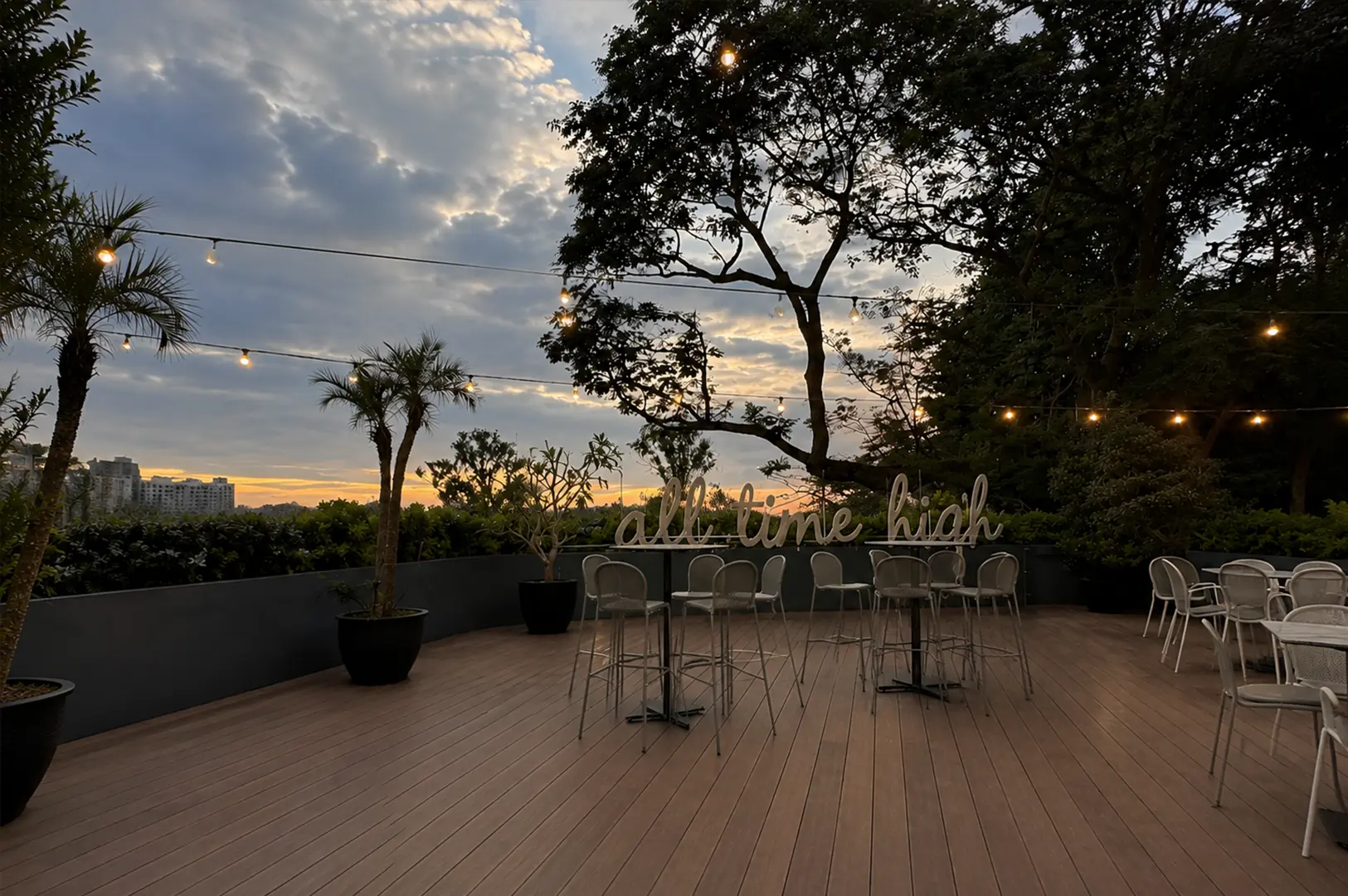 Outdoor terrace at Odette Singapore featuring sunset views, string lights, lush greenery, and elegant seating for guests.