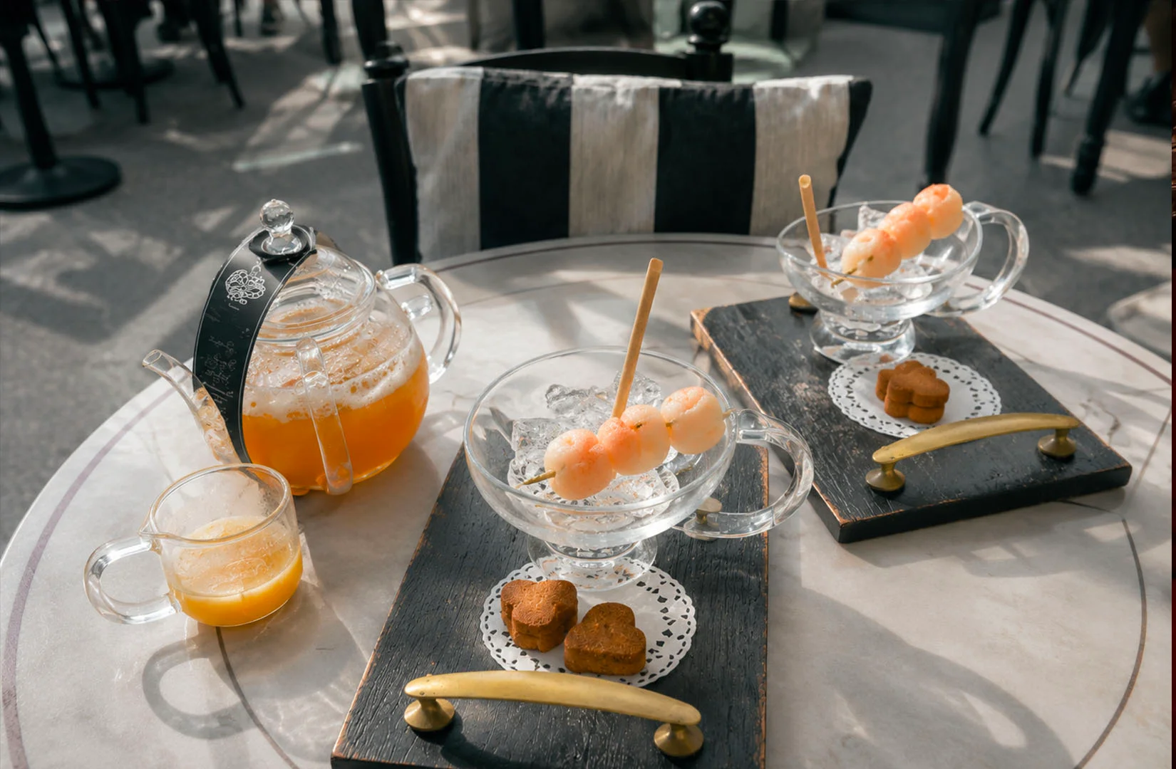Elegant afternoon tea setup with glass teapot, desserts, and small bites arranged on a round table in a bright café setti