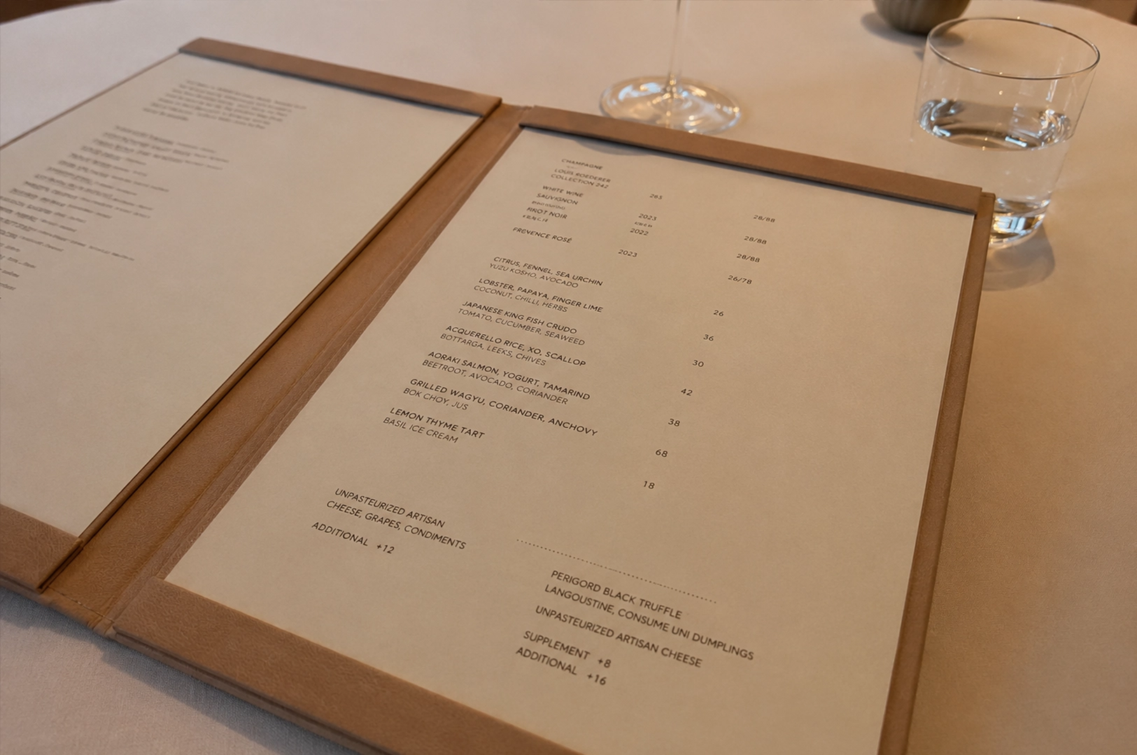 Tasting menu at Odette Singapore displayed on a minimalist leather-bound menu beside wine and table setting.