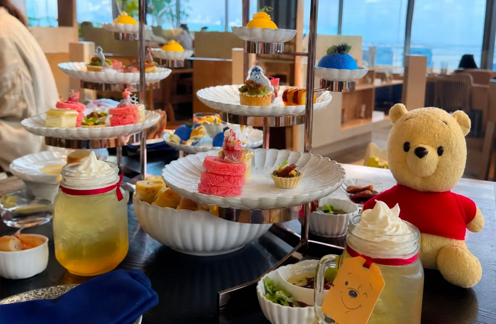 Afternoon tea desserts on tiered trays beside a teddy bear in a cozy cafe setup.