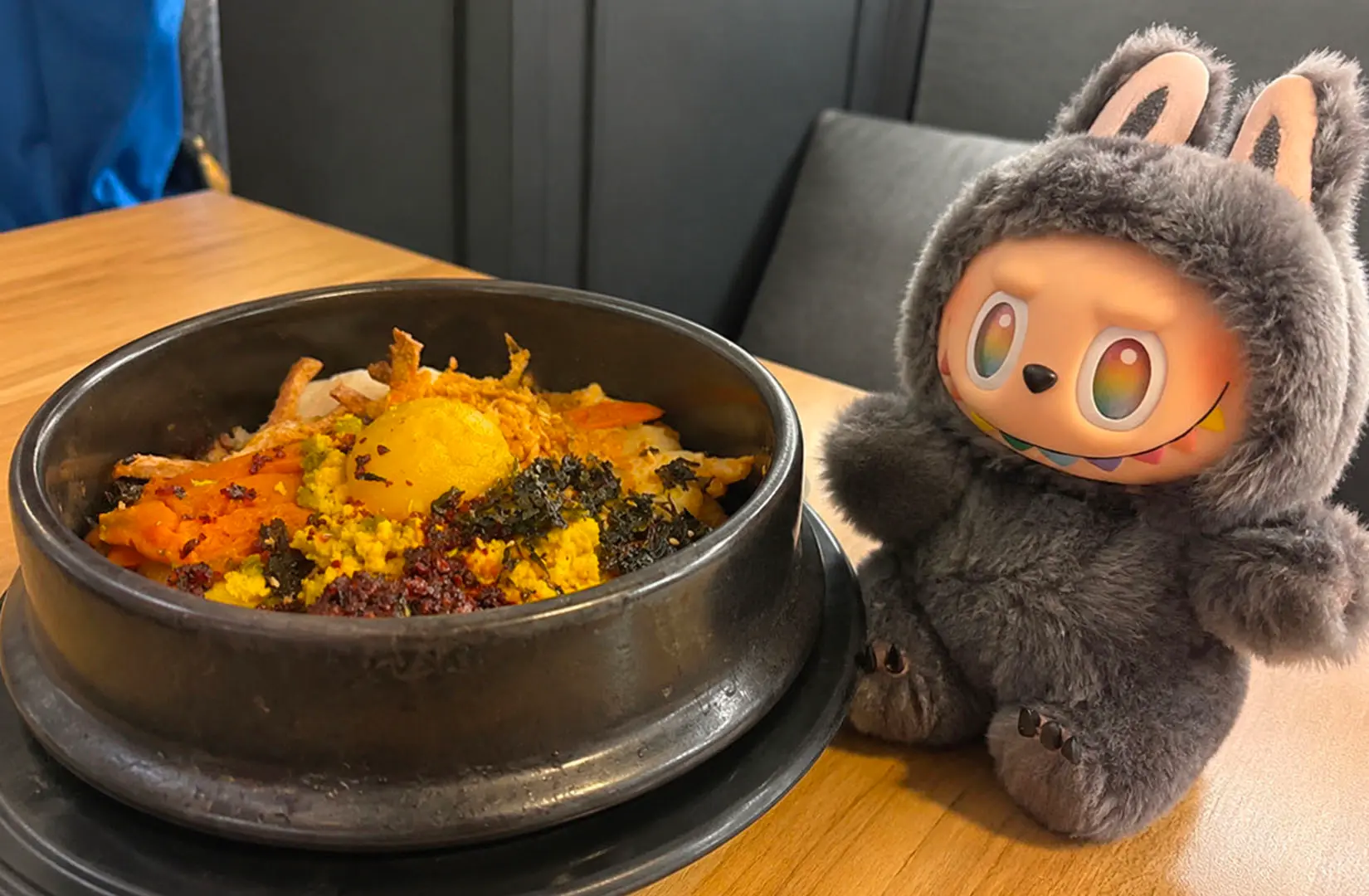 Mixed rice bowl with toppings and a plush character toy in a café setting