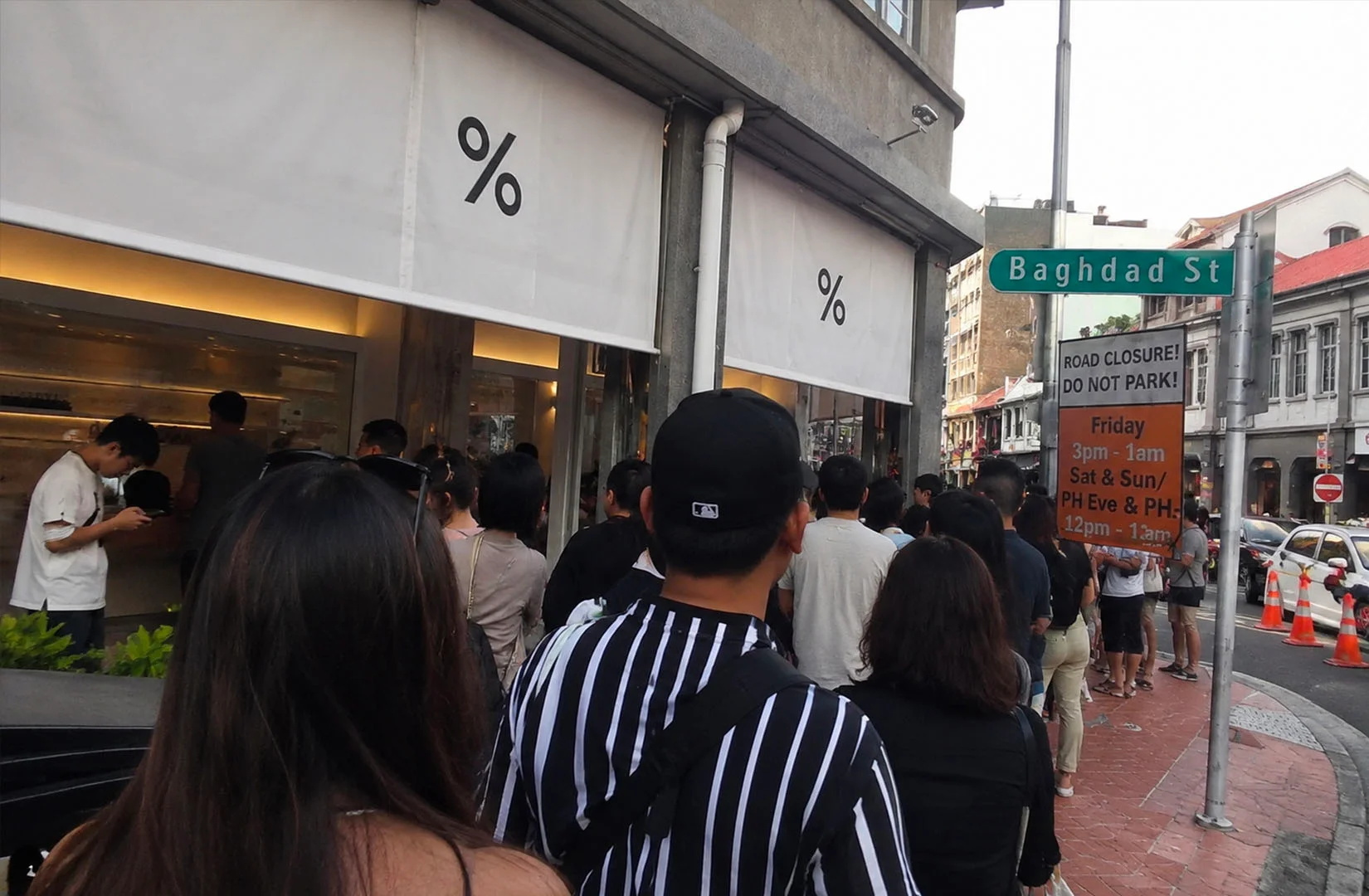Crowd lined up outside a % Arabica café storefront on a city street with signage and queue stretching along the sidewalk