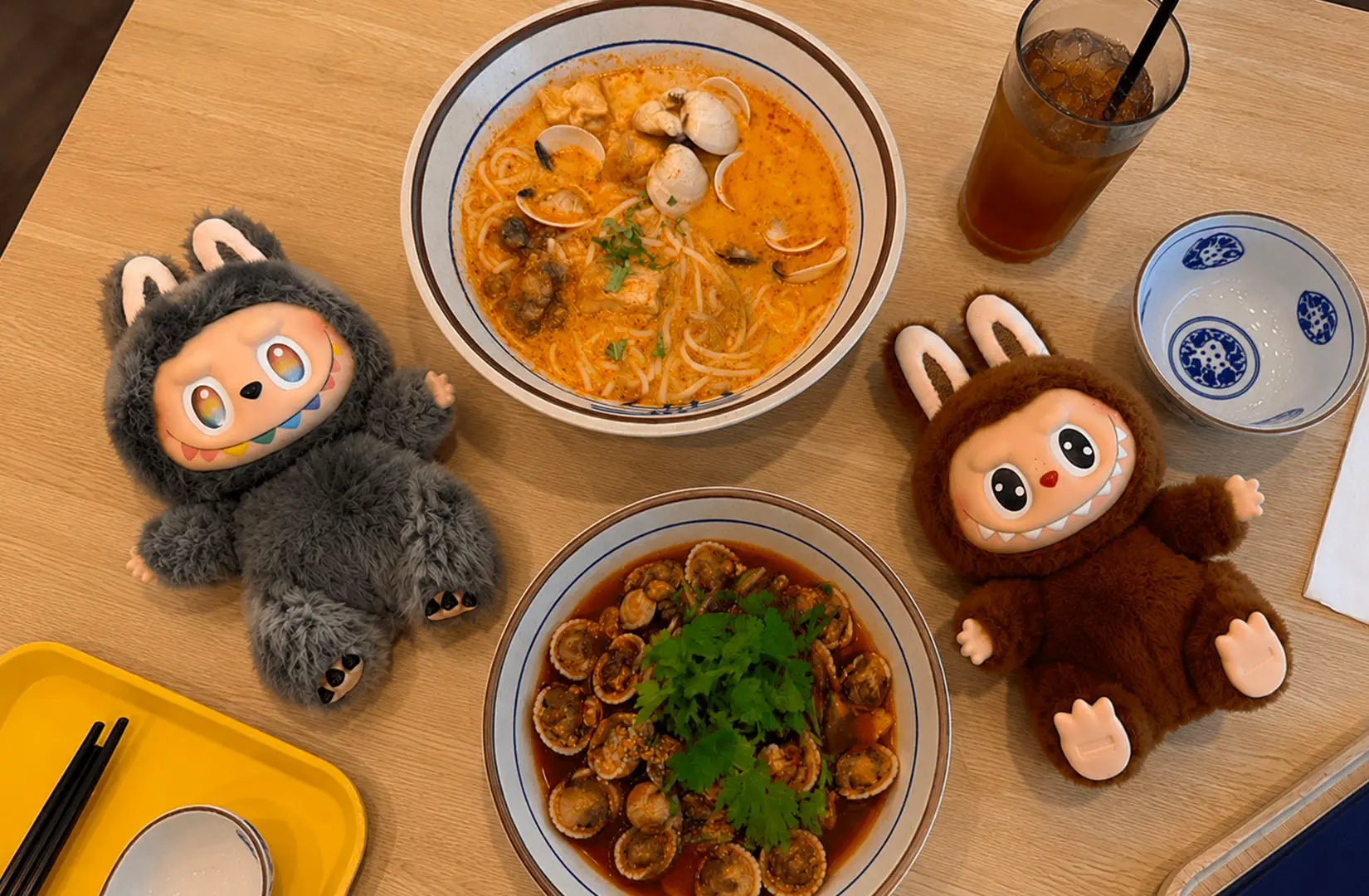 Seafood noodle soup bowls with clams and drinks on a café table with plush toys