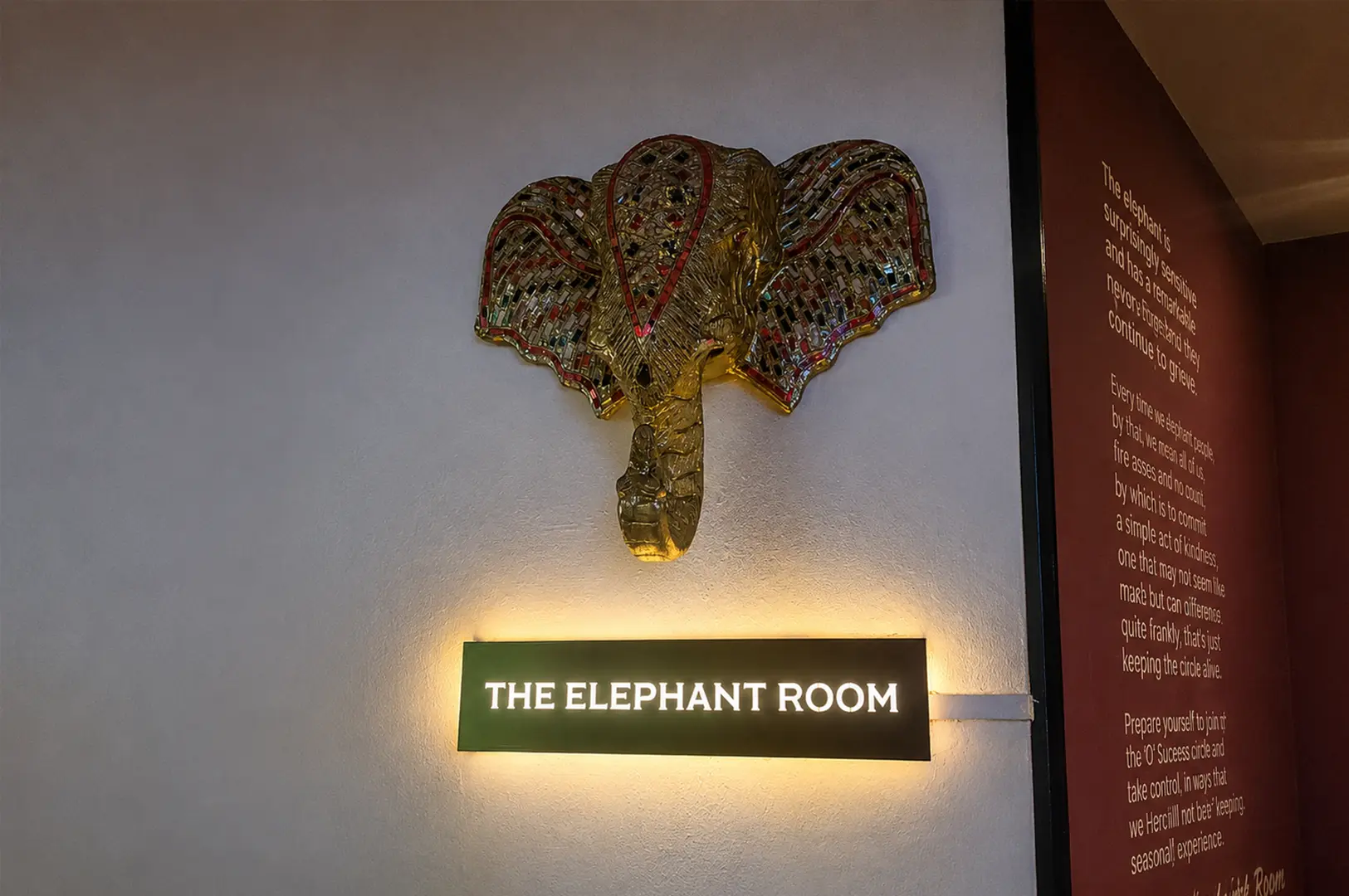 Decorative elephant wall art above the illuminated Elephant Room sign at the entrance.