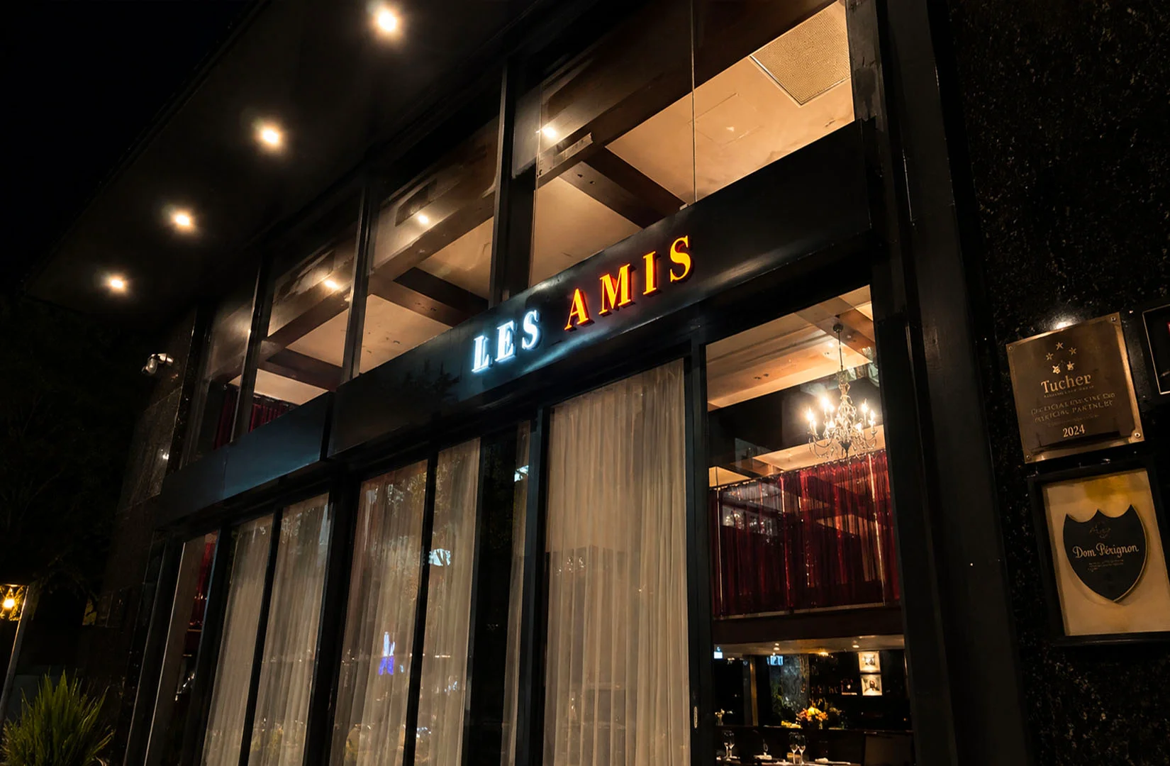 Exterior view of Les Amis fine dining restaurant illuminated at night with elegant glass façade.