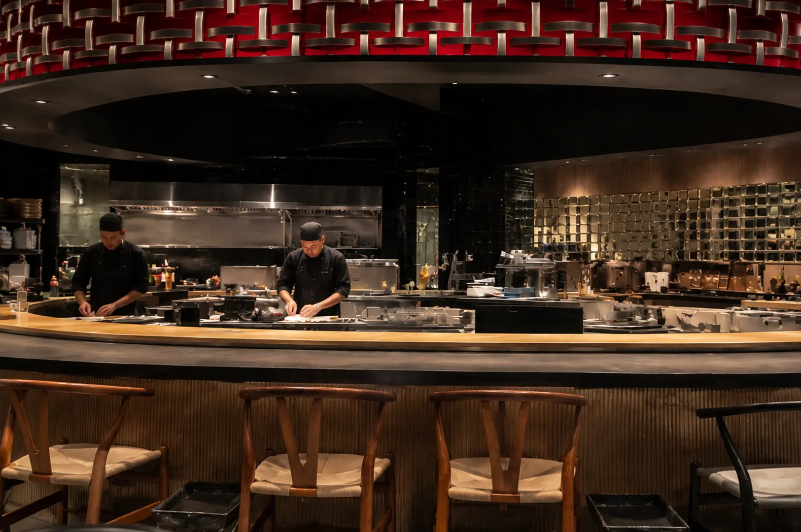 A spacious contemporary sushi restaurant with chefs working behind a long counter, surrounded by dark finishes, warm wood, and decorative lighting at Sen-ryo.