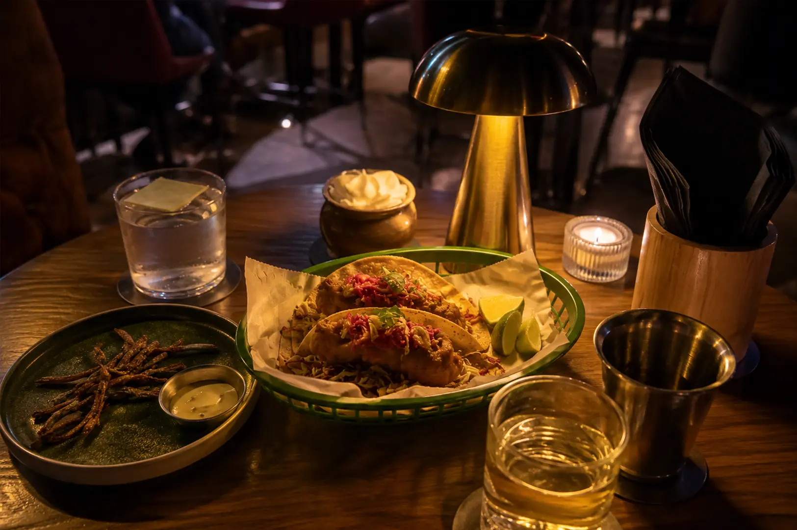 Crispy tacos served with fries, lime wedges, and dipping sauce on a cozy table.