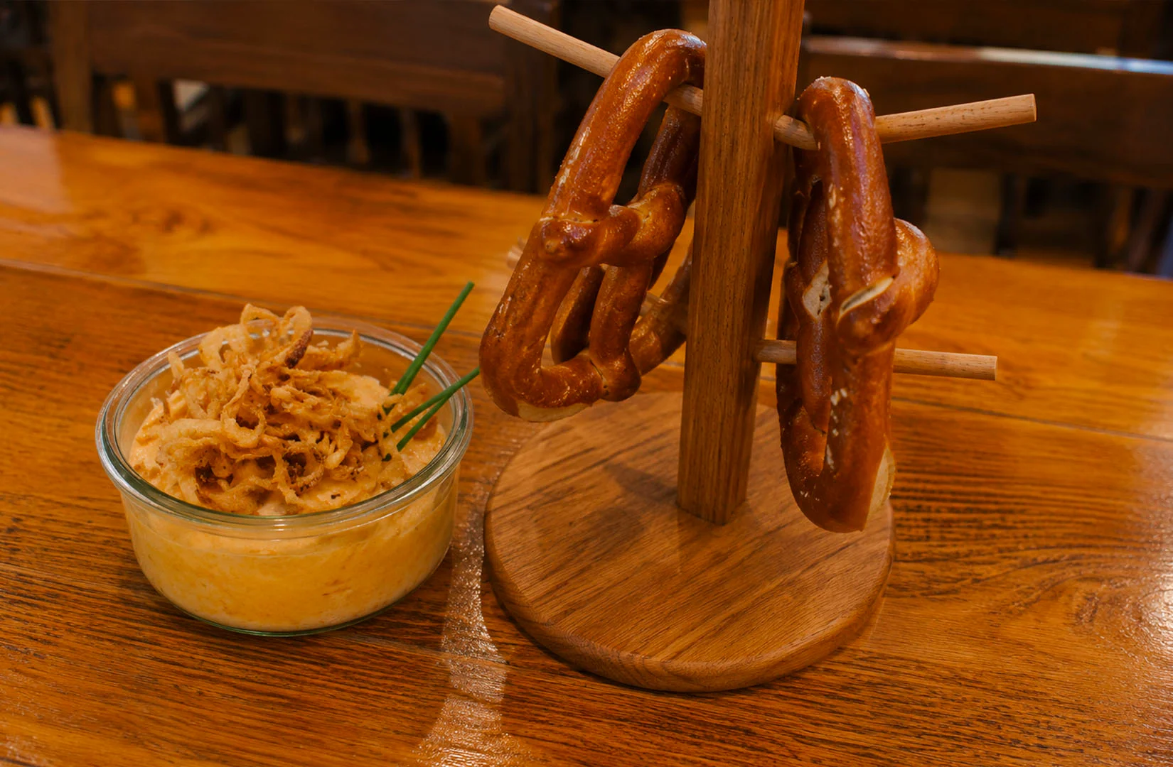 Giant soft pretzels served on a wooden stand with creamy cheese dip topped with crispy fried onions at Paulaner Brauhaus Singapore.