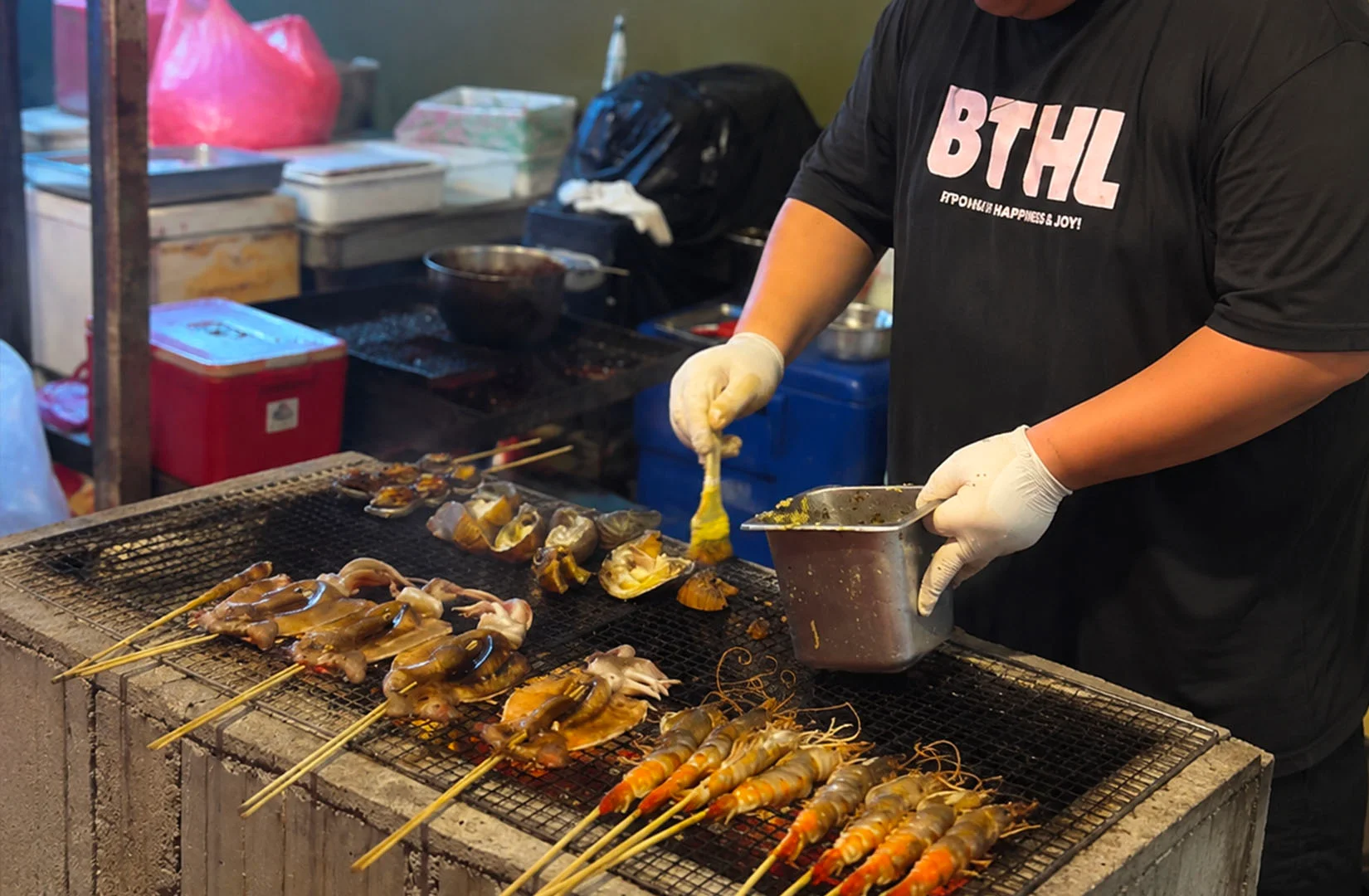 Vendor grilling fresh squid, prawns, and shellfish over charcoal while brushing on savory marinade.