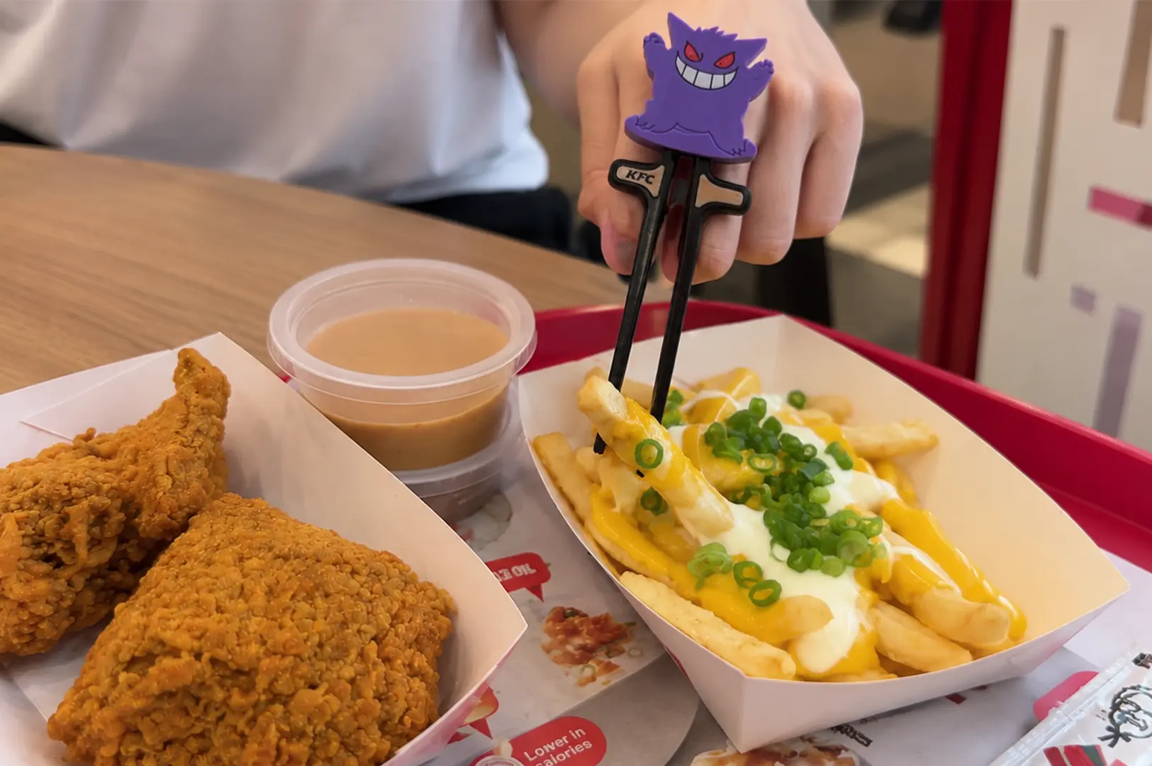 KFC Singapore Pokémon meal featuring crispy fried chicken, loaded cheese fries with green onions, dipping sauce, and a Gengar finger puppet.