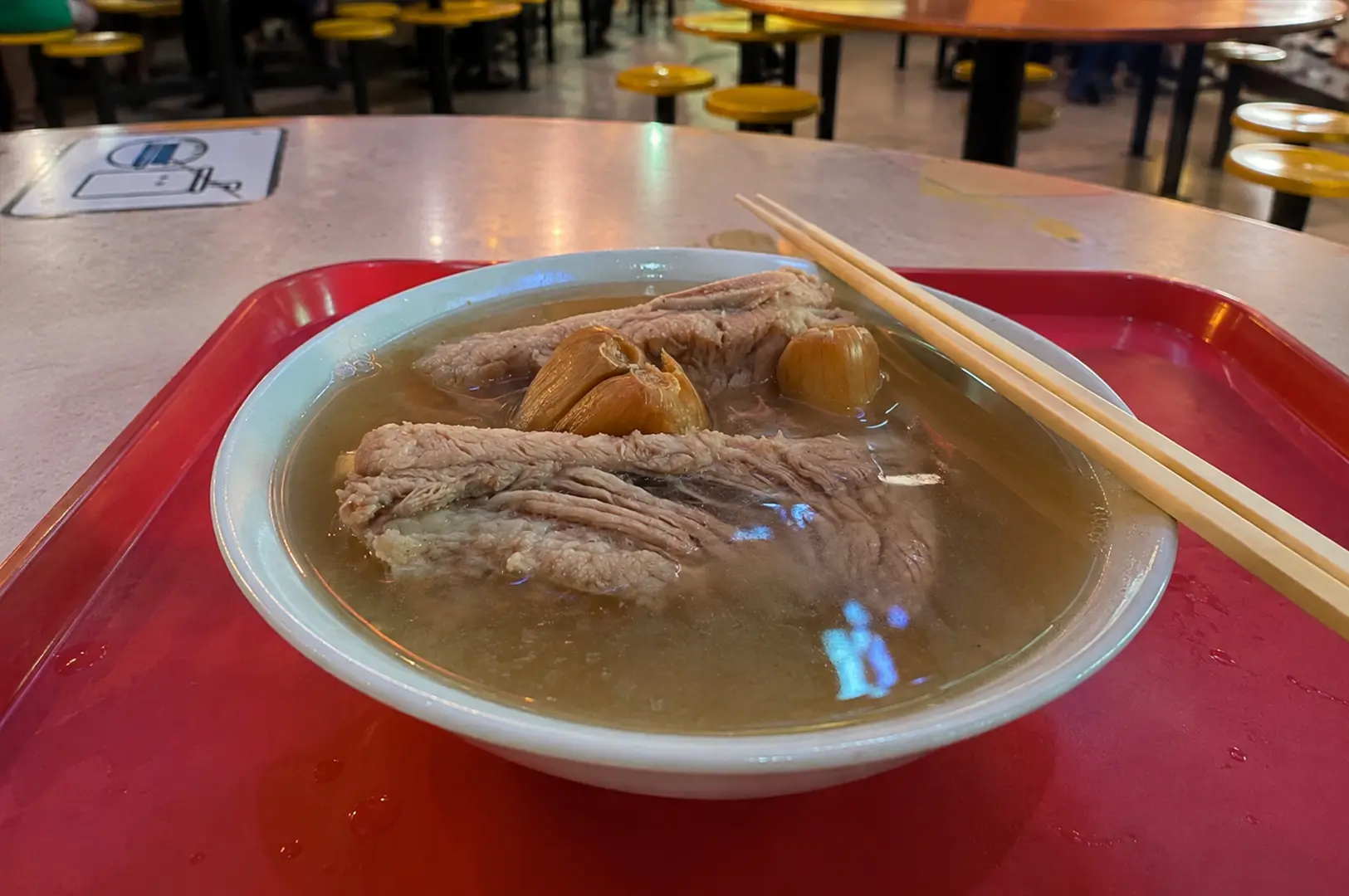 A steaming bowl of Singapore bak kut teh with pork ribs and whole garlic cloves in a clear peppery broth.