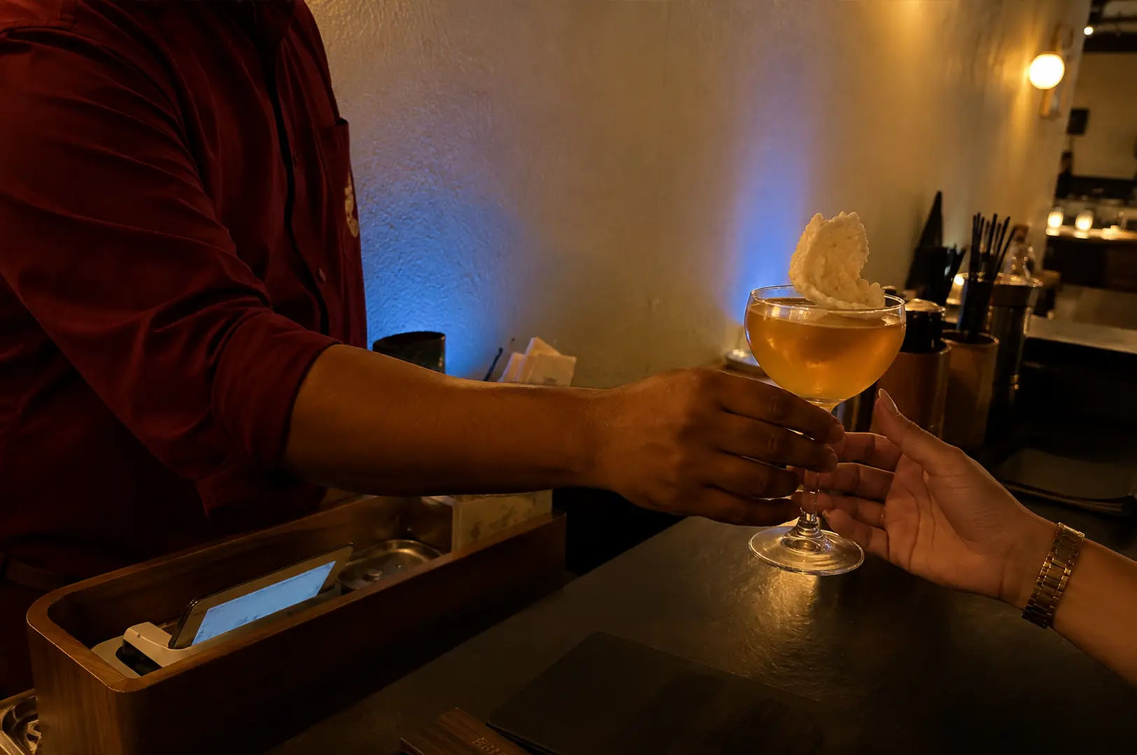 Bartender serving a handcrafted cocktail topped with airy foam to a guest.