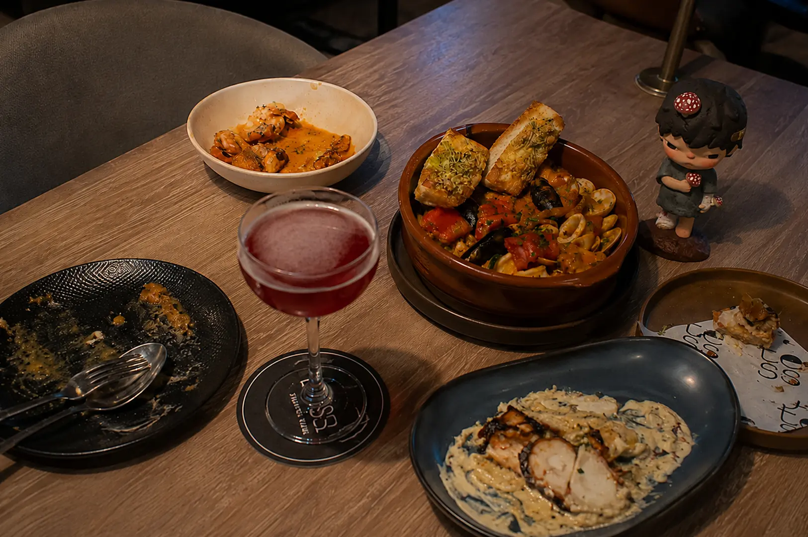 Dining table with seafood dishes, creamy pasta, and a signature cocktail at Tess.