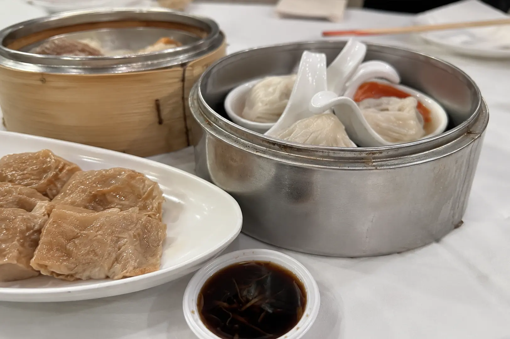 Close-up of steamed dim sum including siu mai and soup dumplings with dipping sauce.