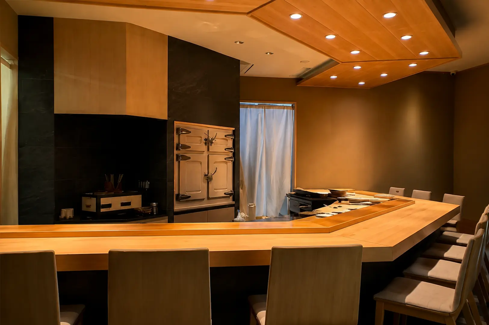 A dark, modern sushi counter with wooden seating, an open kitchen, and a dramatic black textured interior at Sushi Ashino.